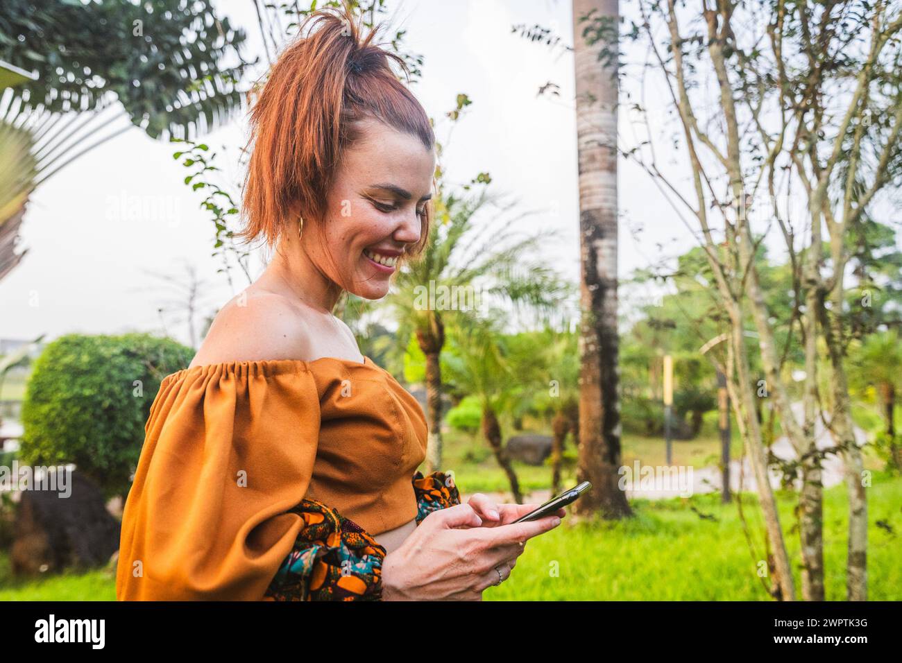 A smiling young woman uses her phone while outside Stock Photo