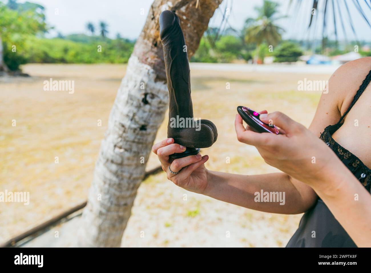 Close-up of a woman trying out a penis-shaped vibrator on a tropical beach Stock Photo