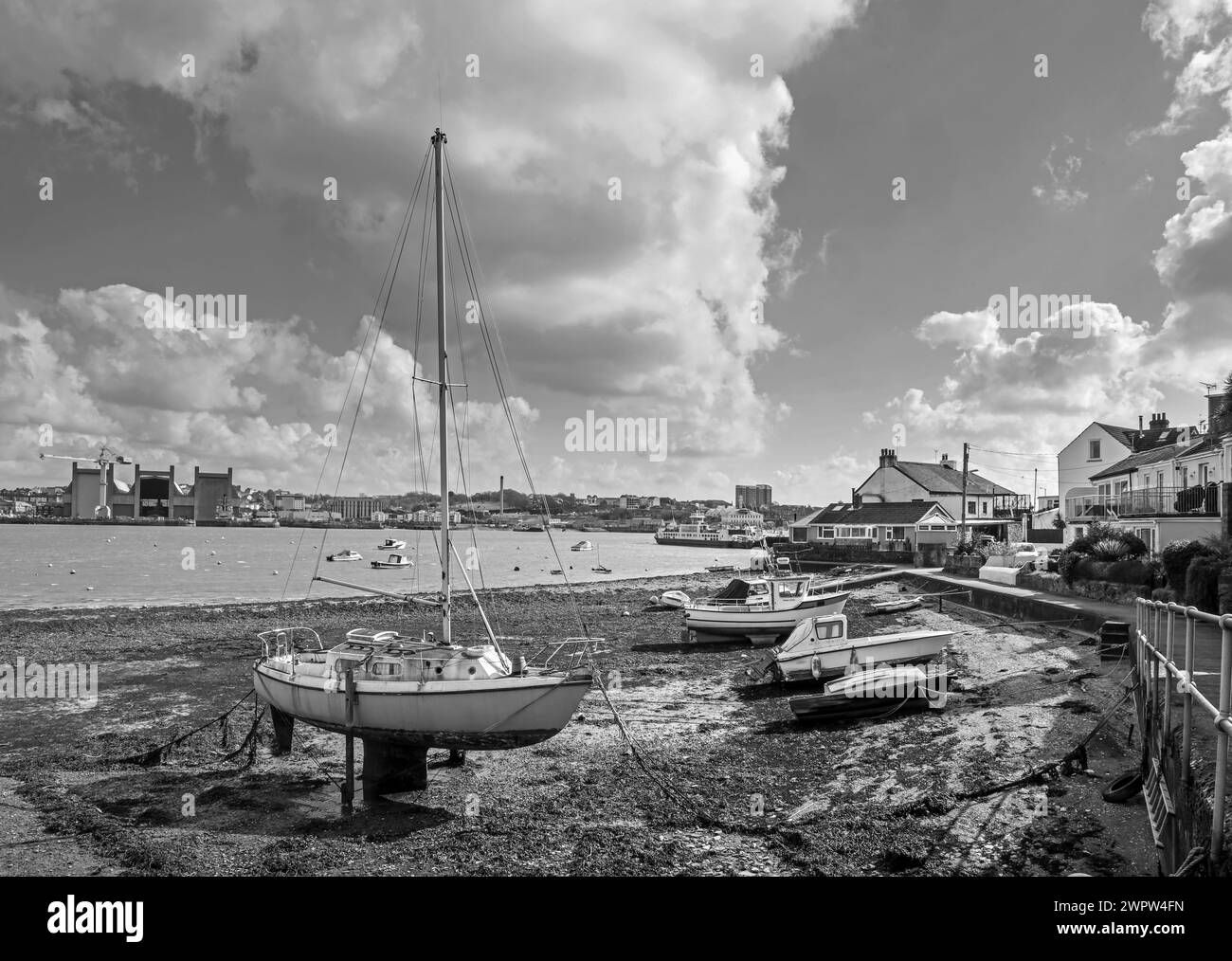 Monochrome image of The riverside at Torpoint in south east Cornwall, with boats berthed on the beach. Across the River Tamar is Devonport Dockyard Stock Photo
