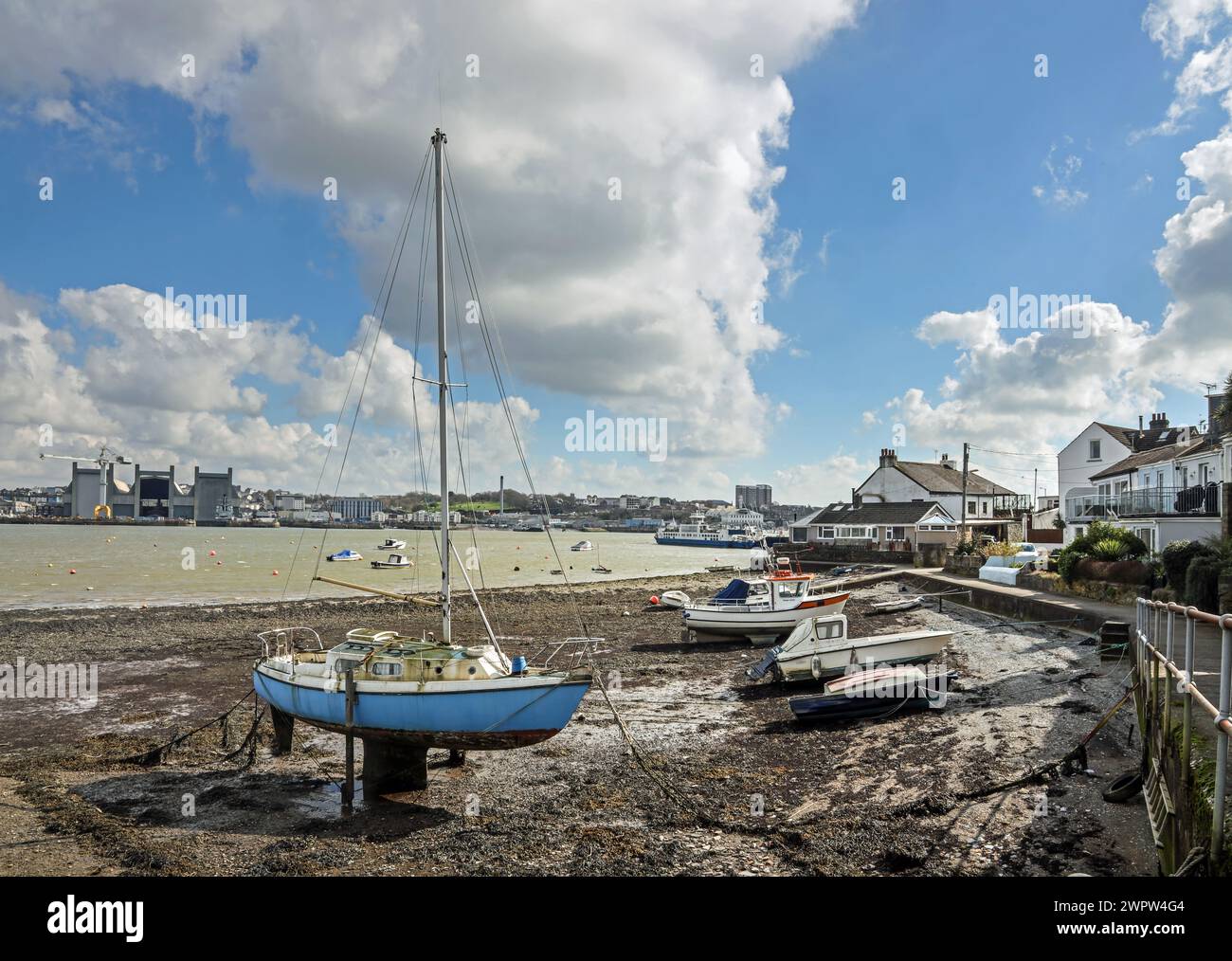 The riverside at Torpoint in south east Cornwall, with boats berthed on the beach. Across the River Tamar is Devonport Dockyard Stock Photo