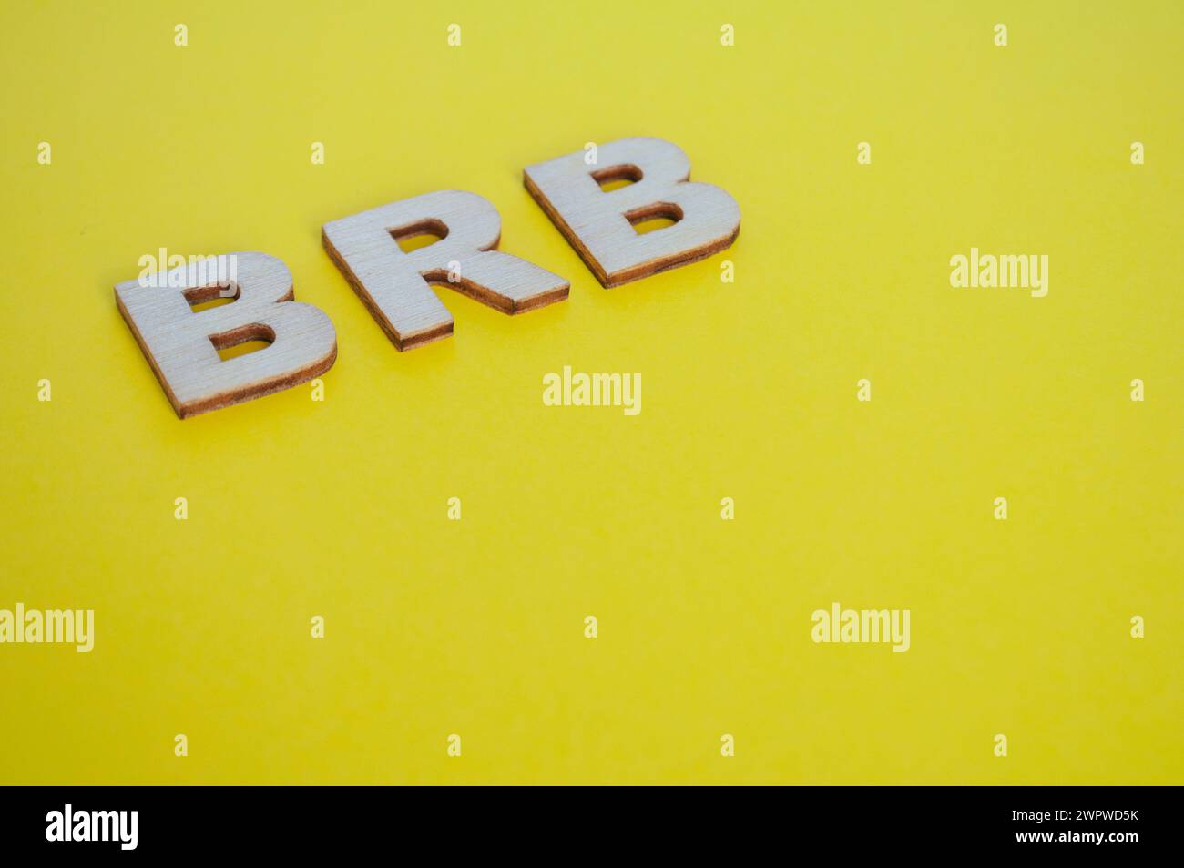 BRB wooden letters representing Be Right Back on yellow background. Stock Photo