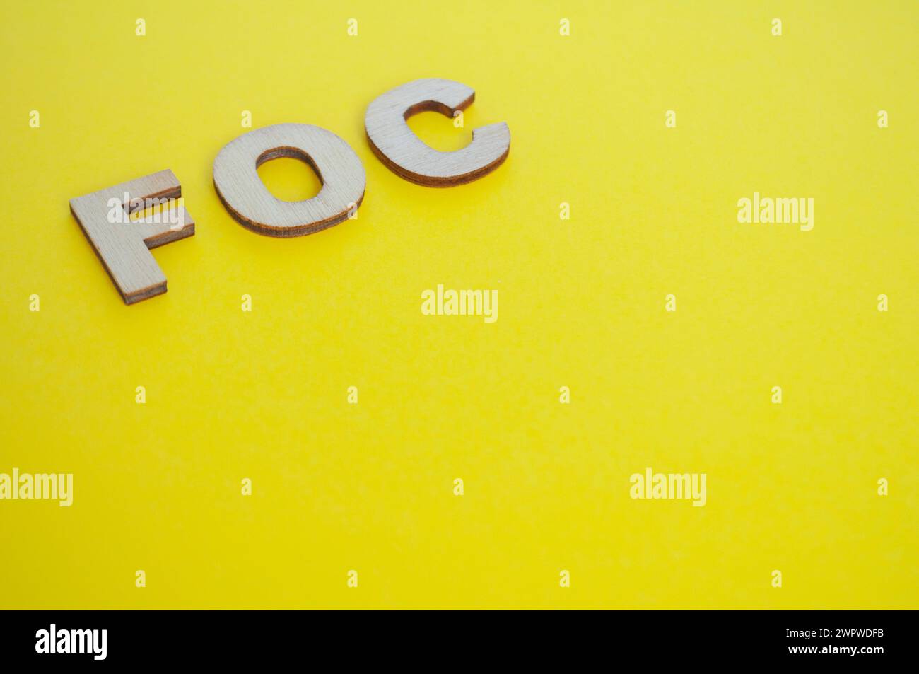 FOC wooden letters representing Free Of Charge on yellow background. Stock Photo