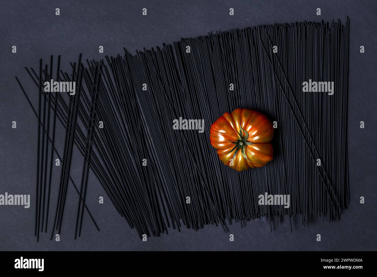 A succulent ripe Raf tomato on a black dyed spaghetti all on a smooth black surface Stock Photo