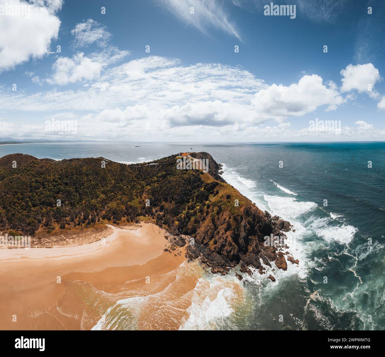 Byron Bay lighthouse high on the rocky headland - the most eastern point of Australian continent facing Pacific ocean in elevated aerial seascape Stock Photo