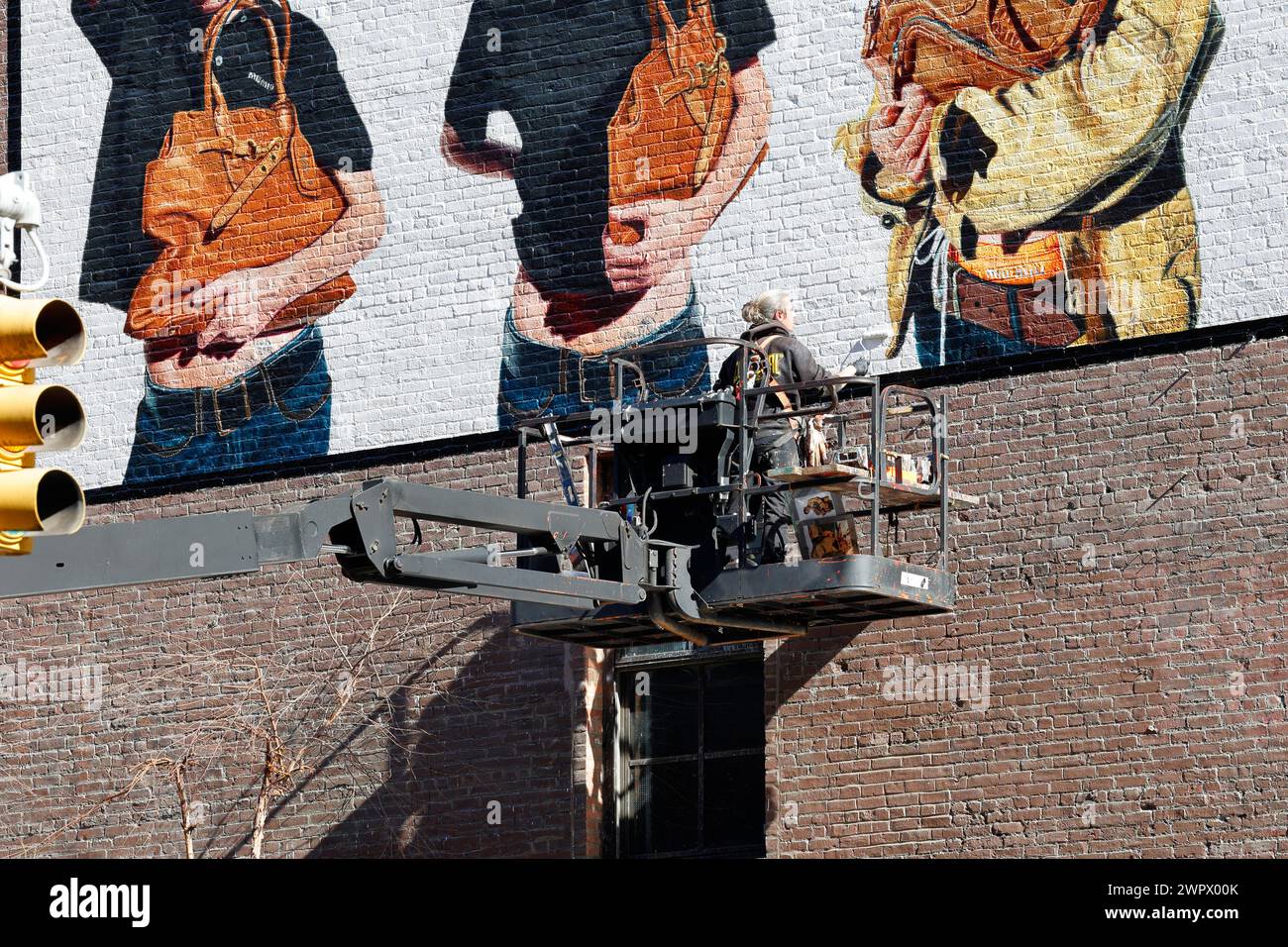 A commercial artist, painters on an articulated boom lift hand painting a billboard advertisement on the side of a building in New York City. Stock Photo