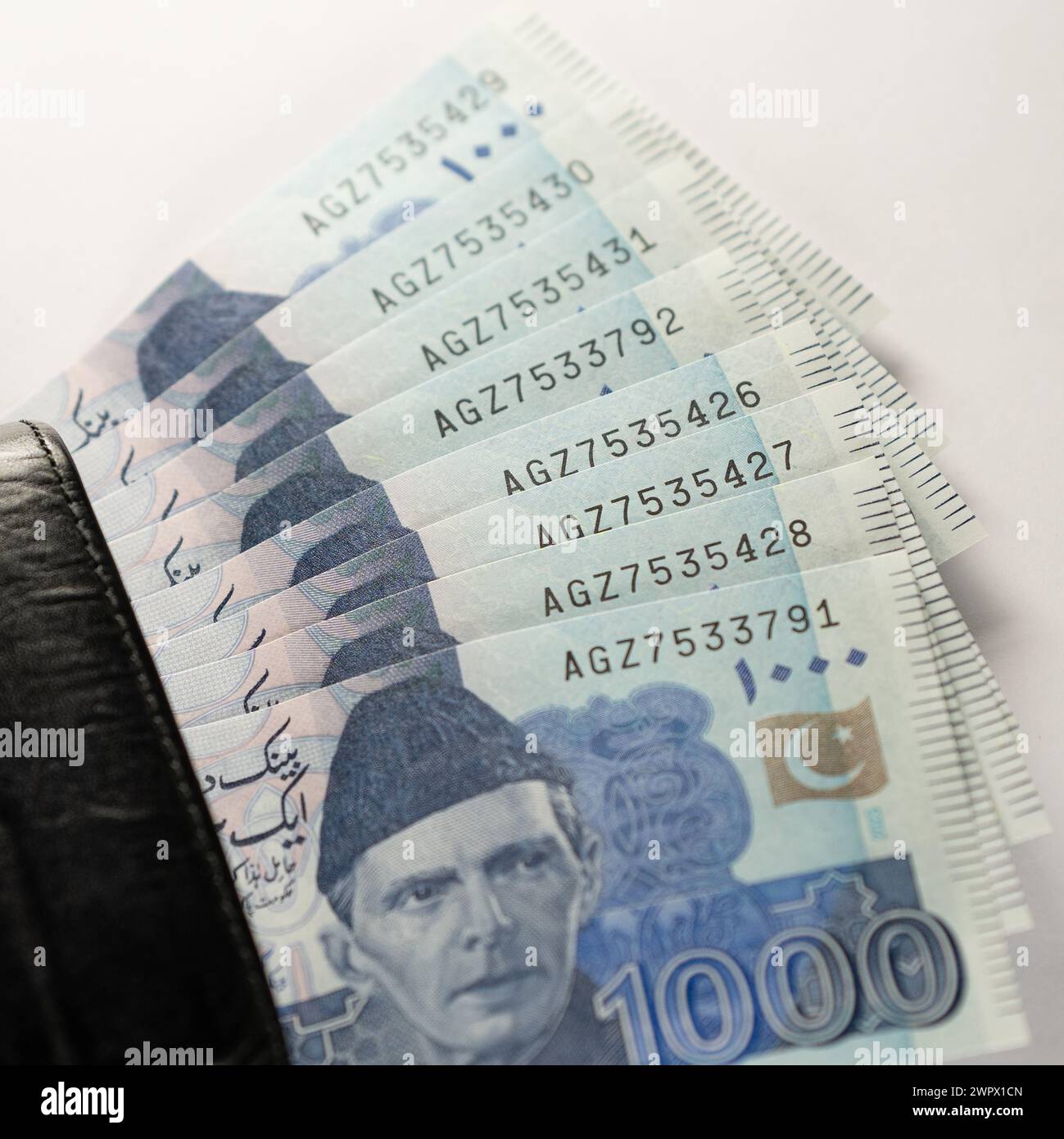 One thousand 1000 rupee bank notes aligned with a black leather wallet. Pakistan State Bank official currency notes 2024 isolated on white background. Stock Photo