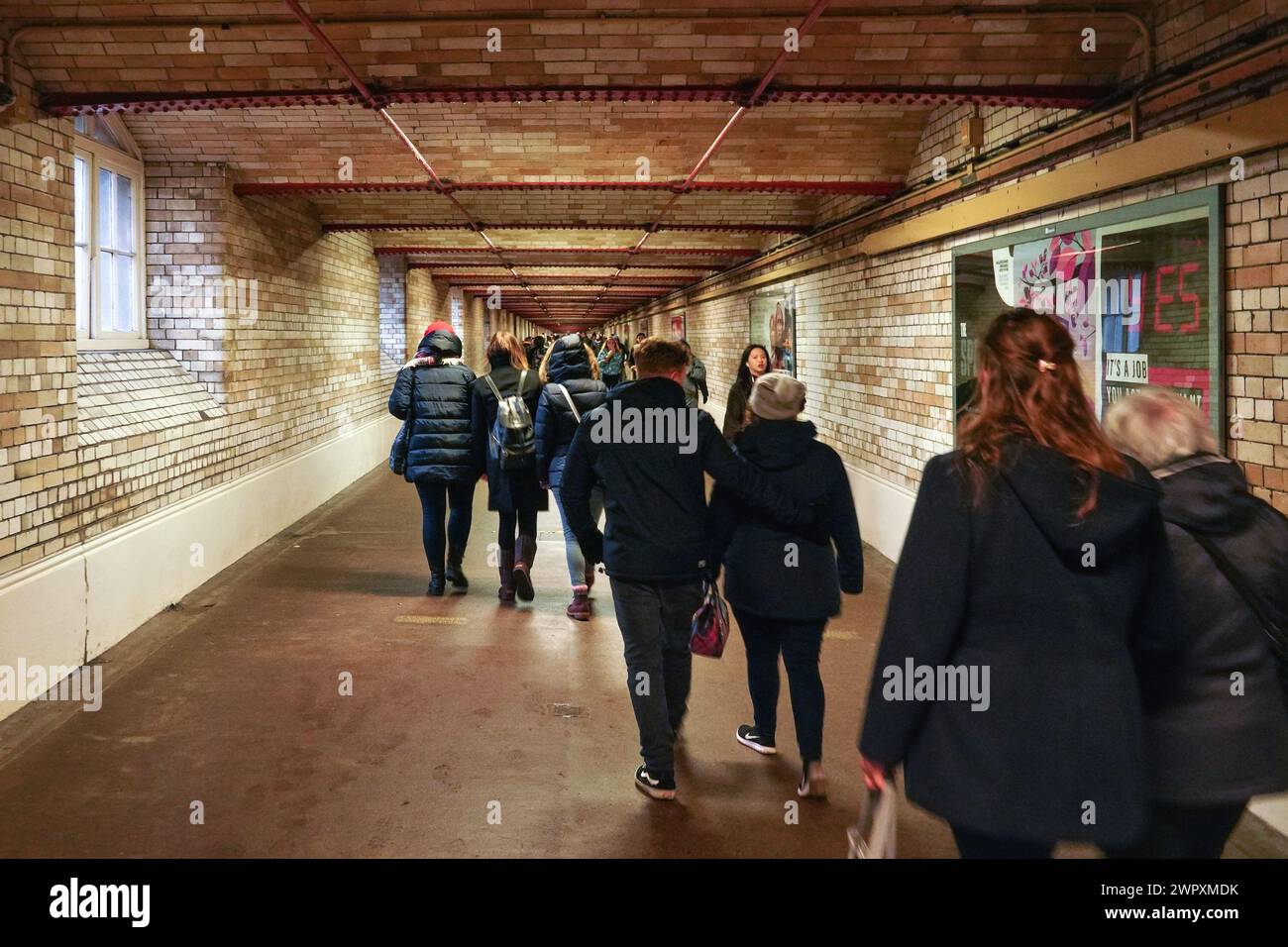 London, United Kingdom - February 01, 2019: Commuters in winter clothes walking through tunnel to Kensington tube station, view from behind Stock Photo