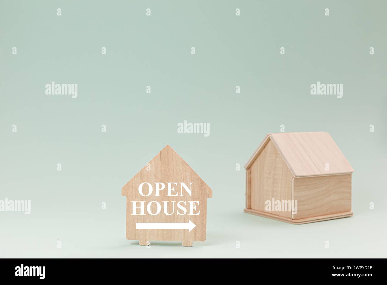 Simplistic wooden house model isolated on pale green background, with text Open House on signboard. Stock Photo