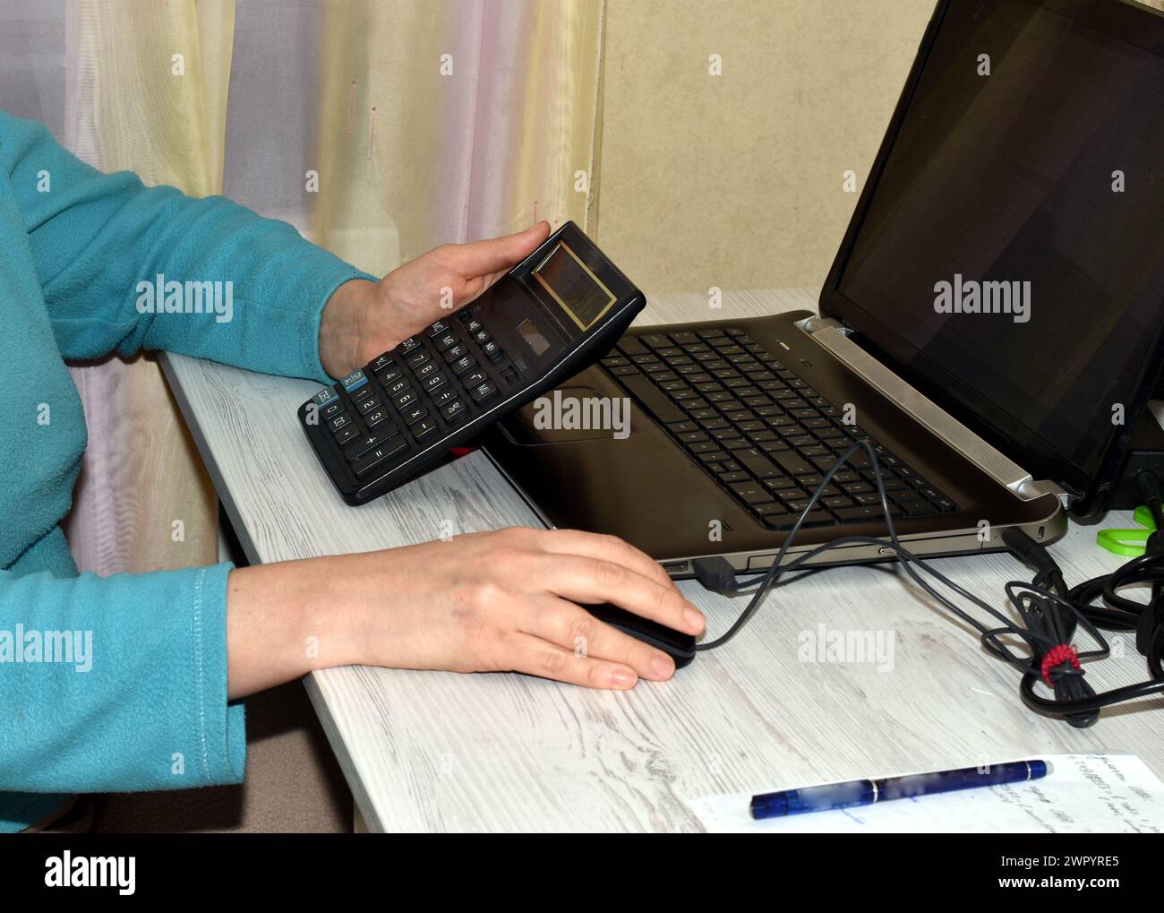 A woman sits in front of an open laptop. He holds a calculator in his hands. She is counting. Stock Photo