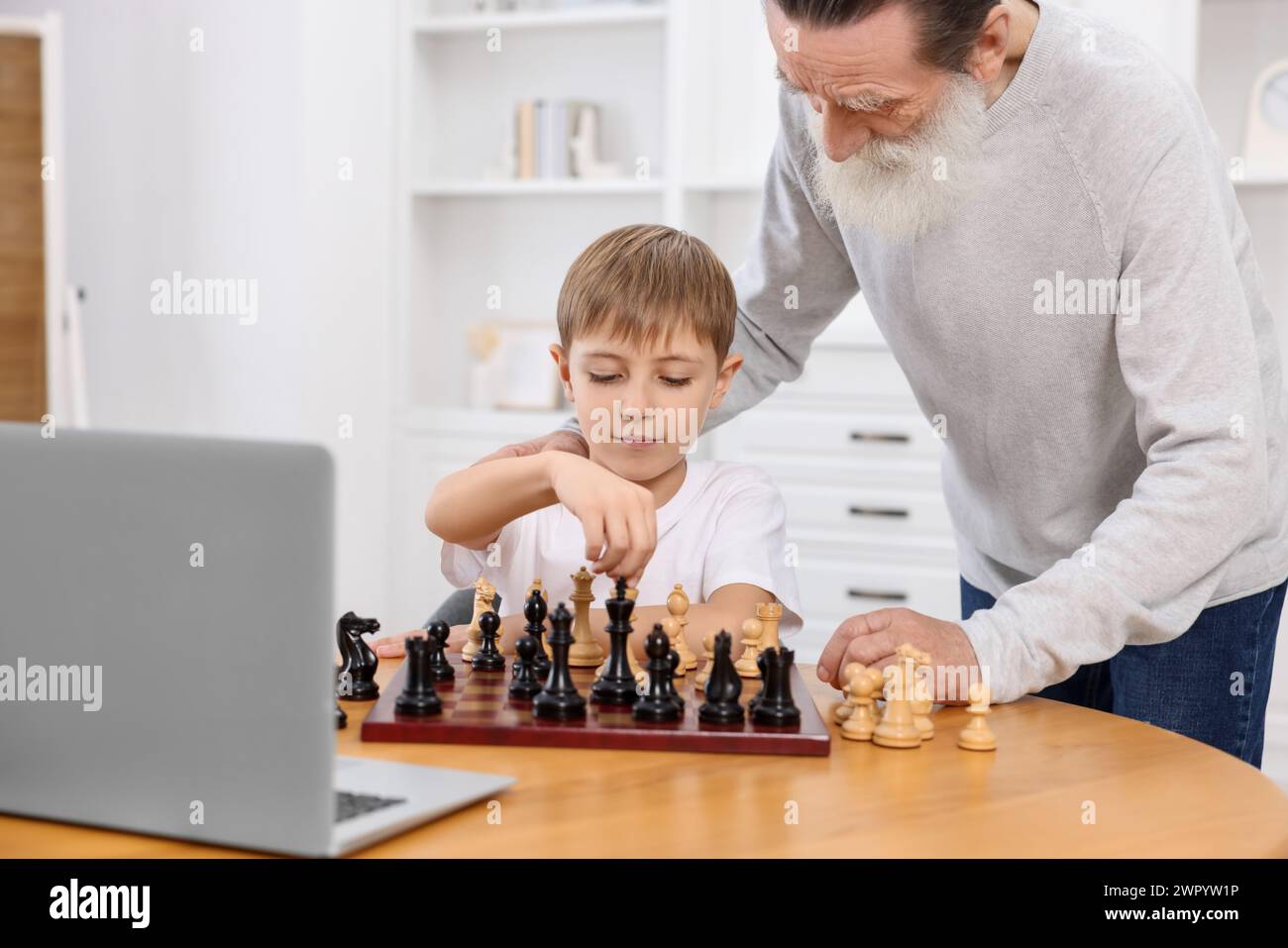 Grandfather teaching his grandson to play chess following online lesson ...
