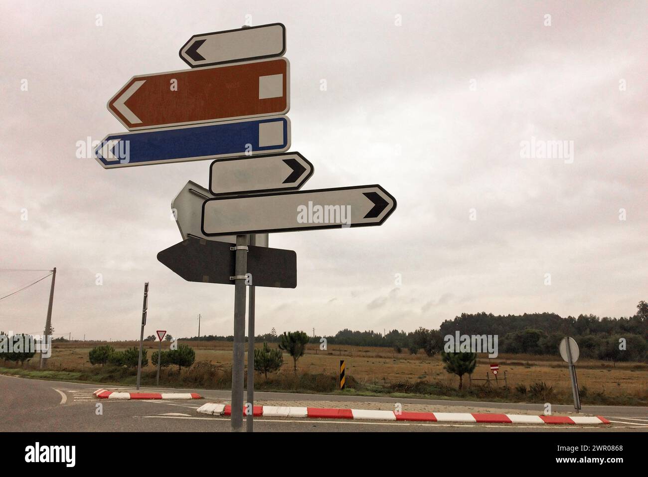 Five empty sign arrows, of different colors, point in various directions at a crossroad. Stock Photo