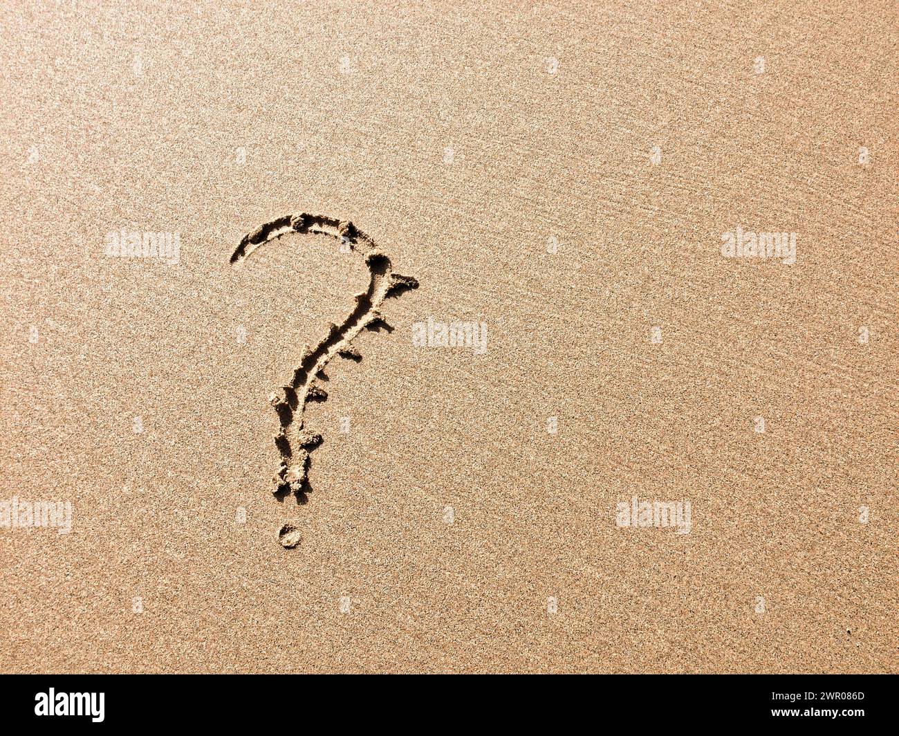 A sandy surface bears a clear question mark, indicating a query or doubt. Stock Photo