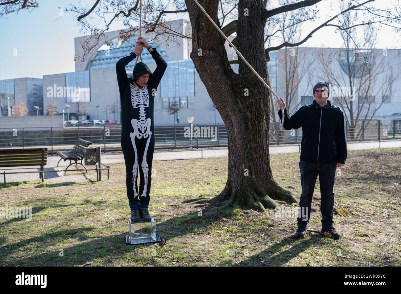 07.03.2024, Berlin, Germany, Europe - Climate activist wears a skeleton costume and stands with a rope around his neck on a block of ice. Stock Photo