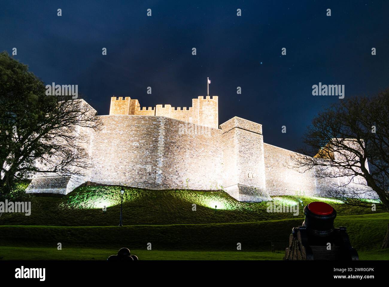 Dover castle at night. The embankment and curtain wall surrounding the main keep illuminated by spotlights. Medieval mortar in the foreground. Stock Photo