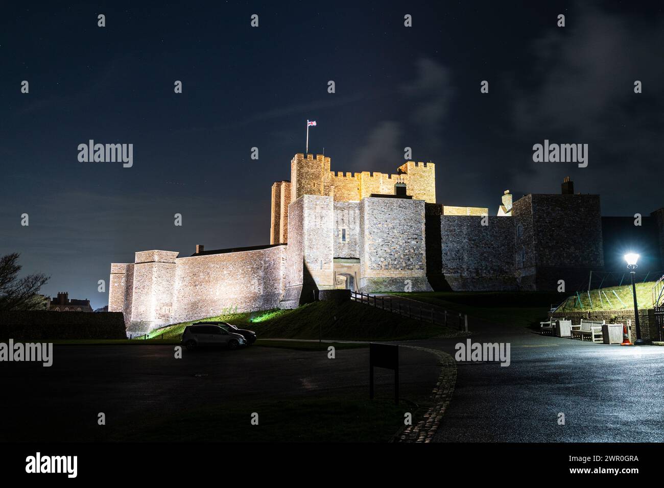Dover castle at night, the main gate in the curtain wall surrounding the Great Keep. Walls illuminated, with the keep behind and Union Jack fluttering Stock Photo
