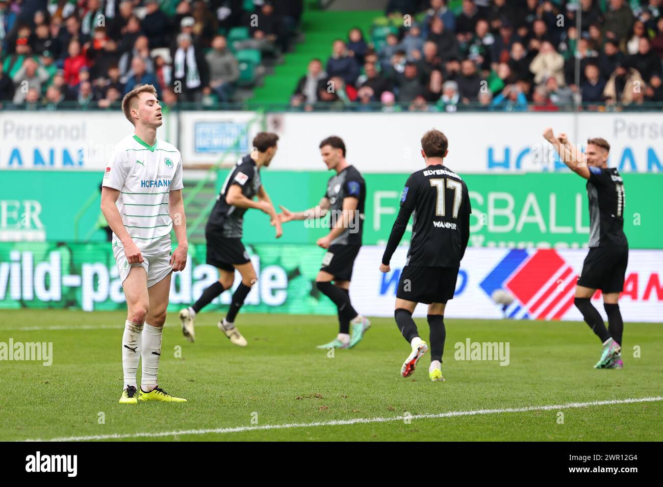 10 March 2024, Bavaria, Fürth: Soccer, Bundesliga 2, SpVgg Greuther Fürth - SV Elversberg, matchday 25 at Sportpark Ronhof Thomas Sommer. Fürth's Gian-Luca Itter (l) stands on the pitch while Paul Stock (2nd from left) from Elversberg celebrates his goal to make it 1-2 with his colleagues. Photo: Daniel Karmann/dpa - IMPORTANT NOTE: In accordance with the regulations of the DFL German Football League and the DFB German Football Association, it is prohibited to utilize or have utilized photographs taken in the stadium and/or of the match in the form of sequential images and/or video-like photo Stock Photo