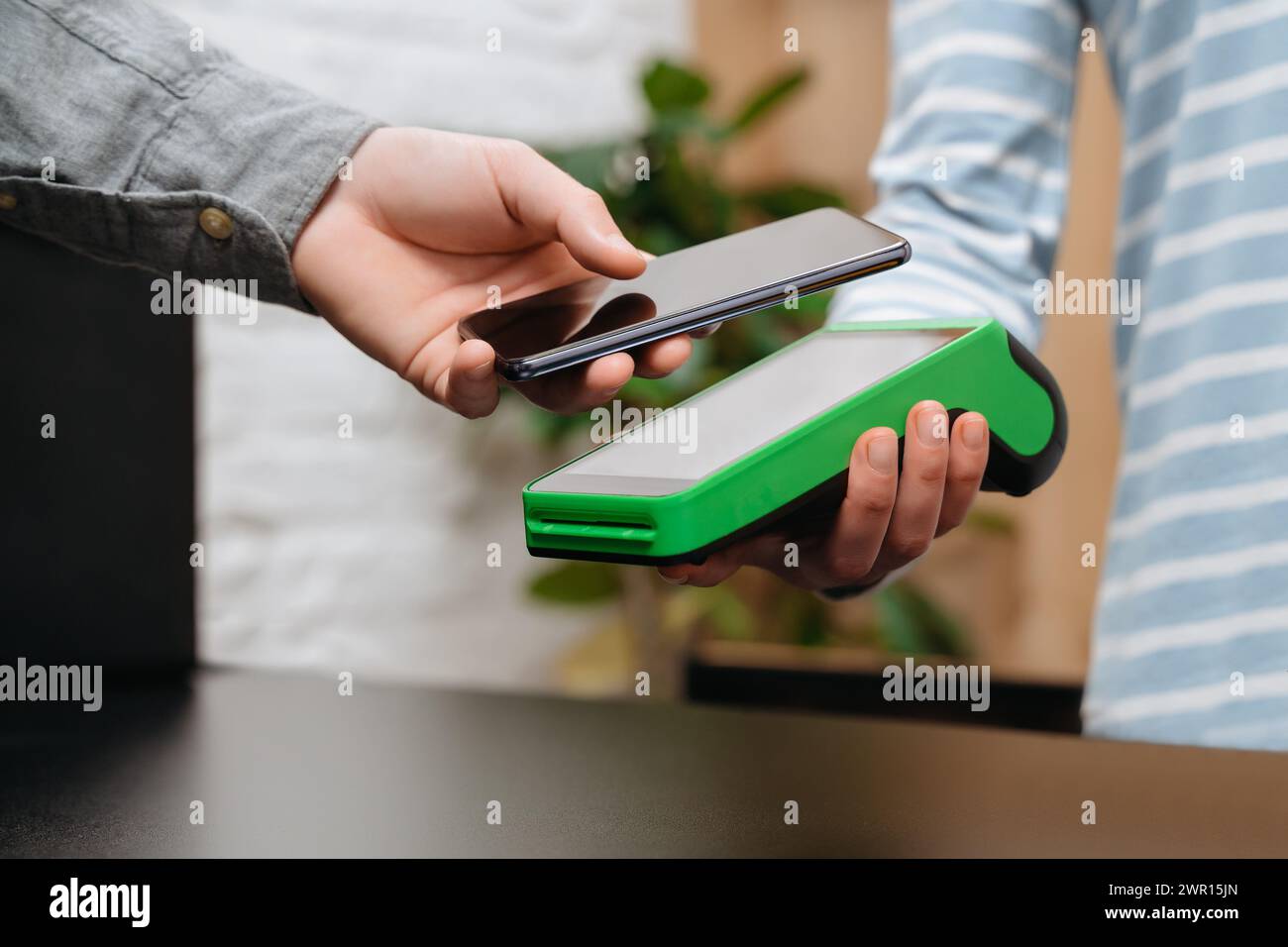 Customer is paying with smartphone in shop using NFC technology. Man doing shopping, buying goods using phone for contactless payment. Contactless and NFC technology Stock Photo
