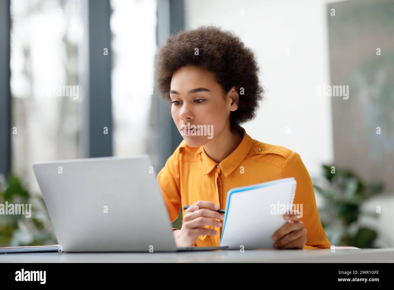 Focused young black woman studying with laptop and notebook Stock Photo ...