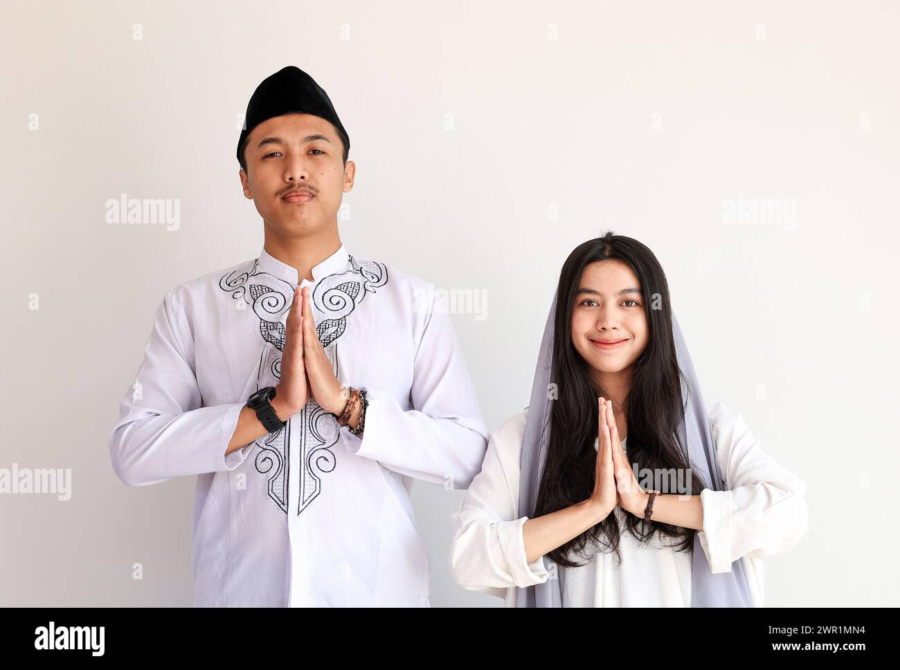 Asian Muslim Male and Female Doing Hari Raya Lebaran Greeting Gesture.  Eid Al Fitr Concept. Isolated on White with Copy Space for Text Stock Photo