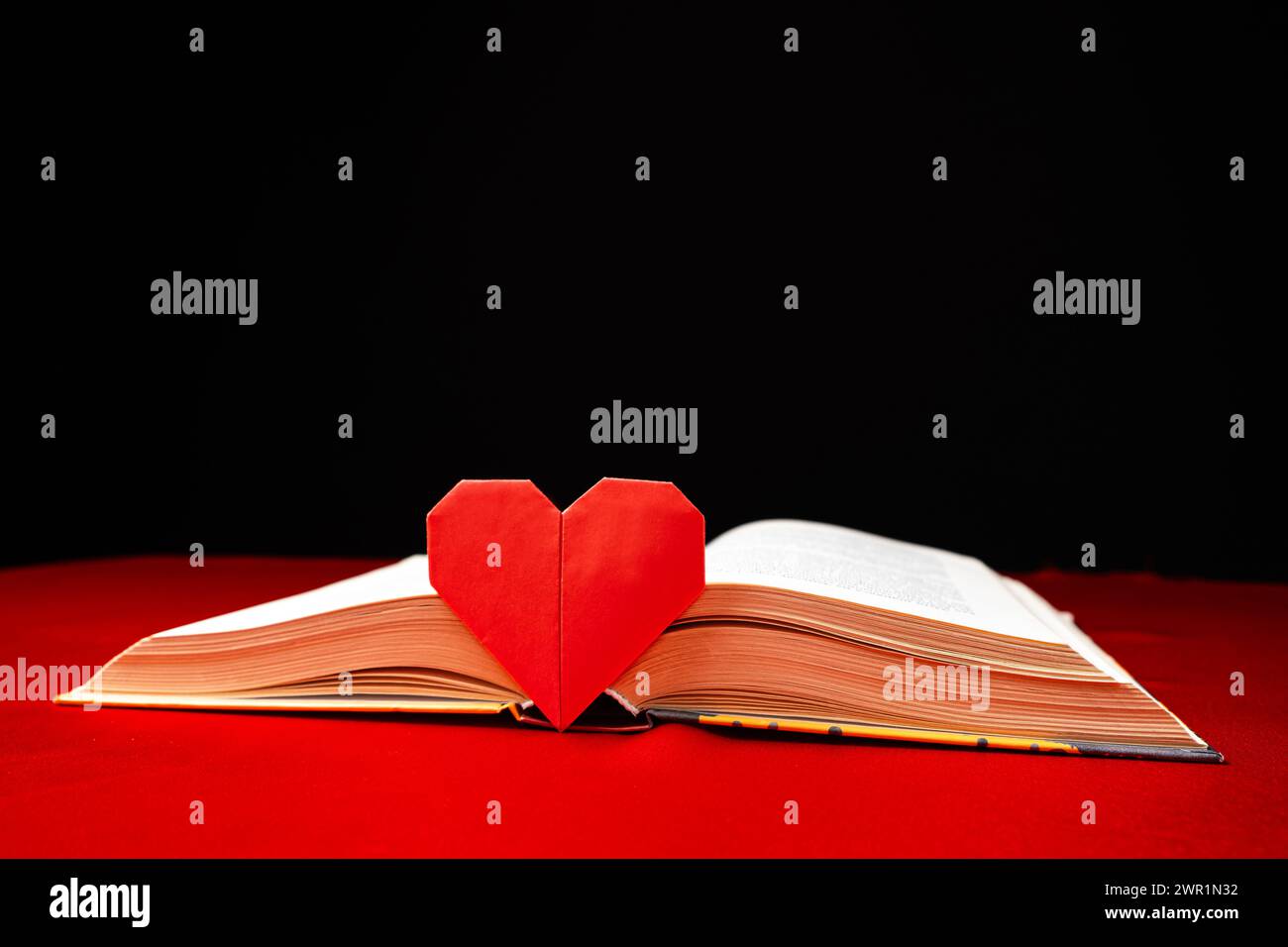 Origami paper heart and thick book on red and black background. Love for books. Stock Photo