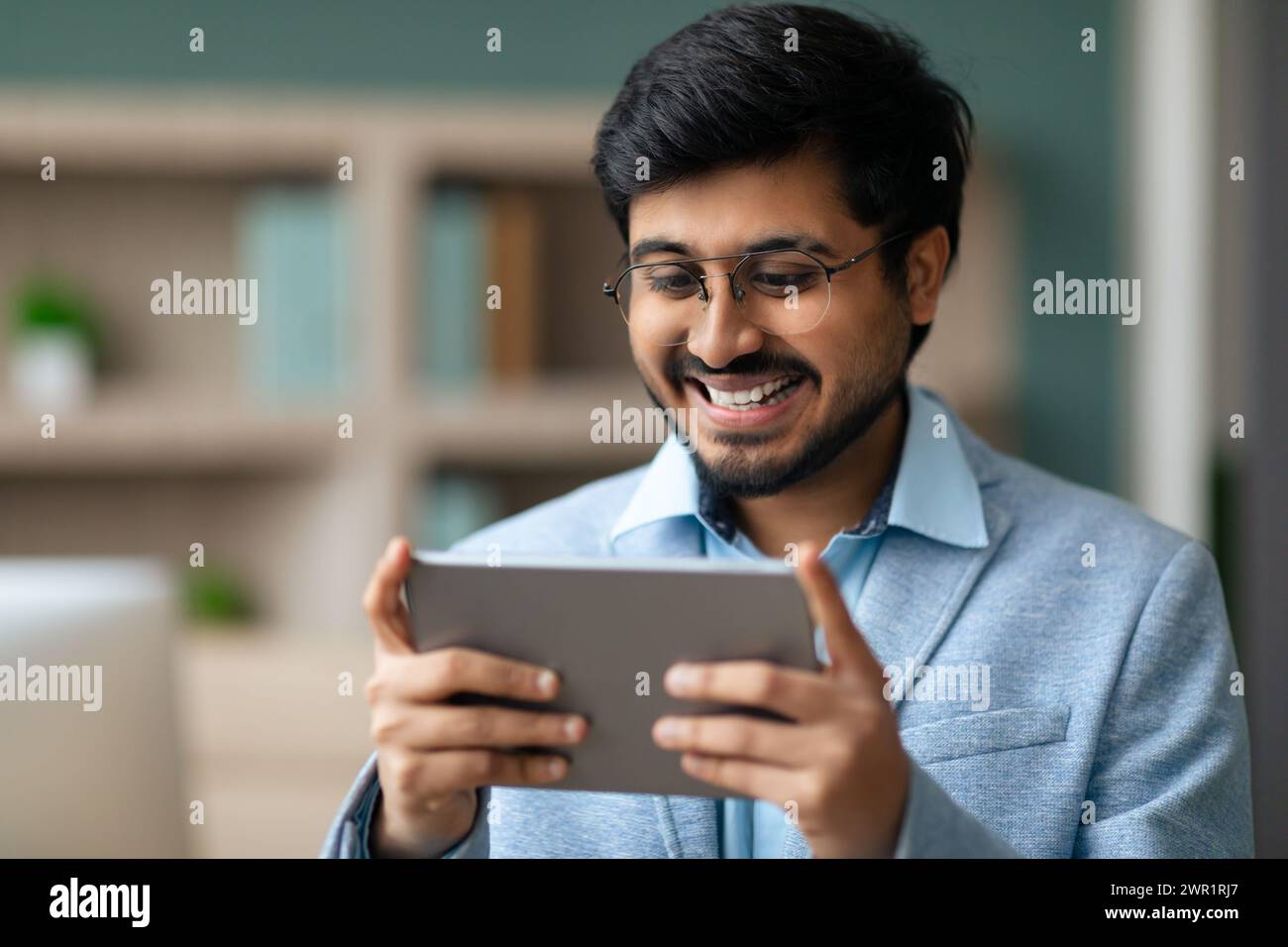 Indian businessman smiles while using application on digital tablet indoor Stock Photo