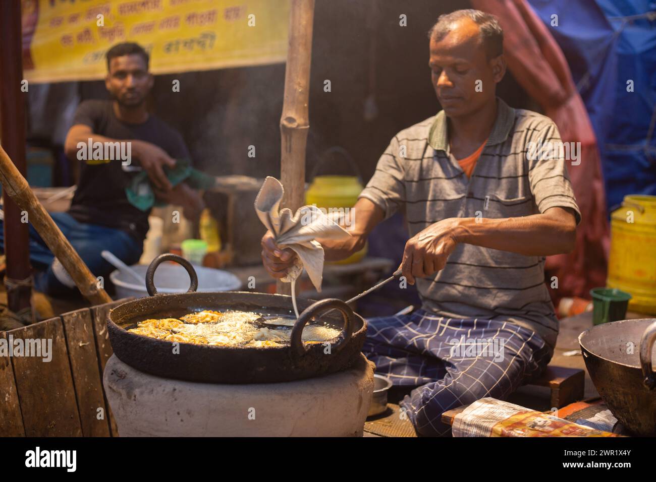 Birbhum, West Bengal, India - February 26th 2024: An Indian shopkeeper at mela or rural fair frying sweets jalebi in oil Stock Photo