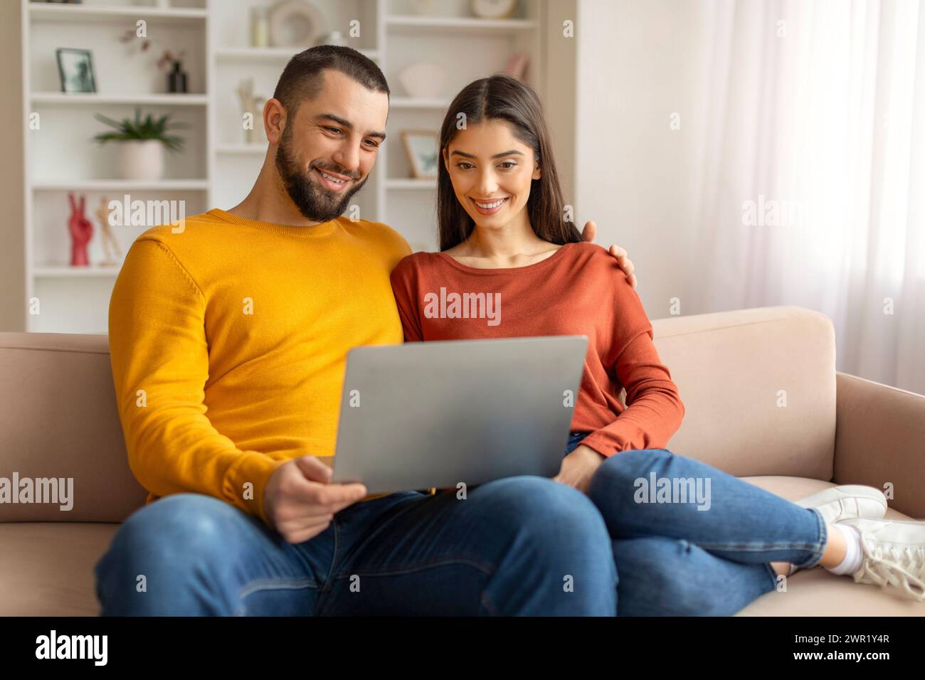 Technologies For Leisure. Happy Young Couple Using Laptop Together At Home Stock Photo