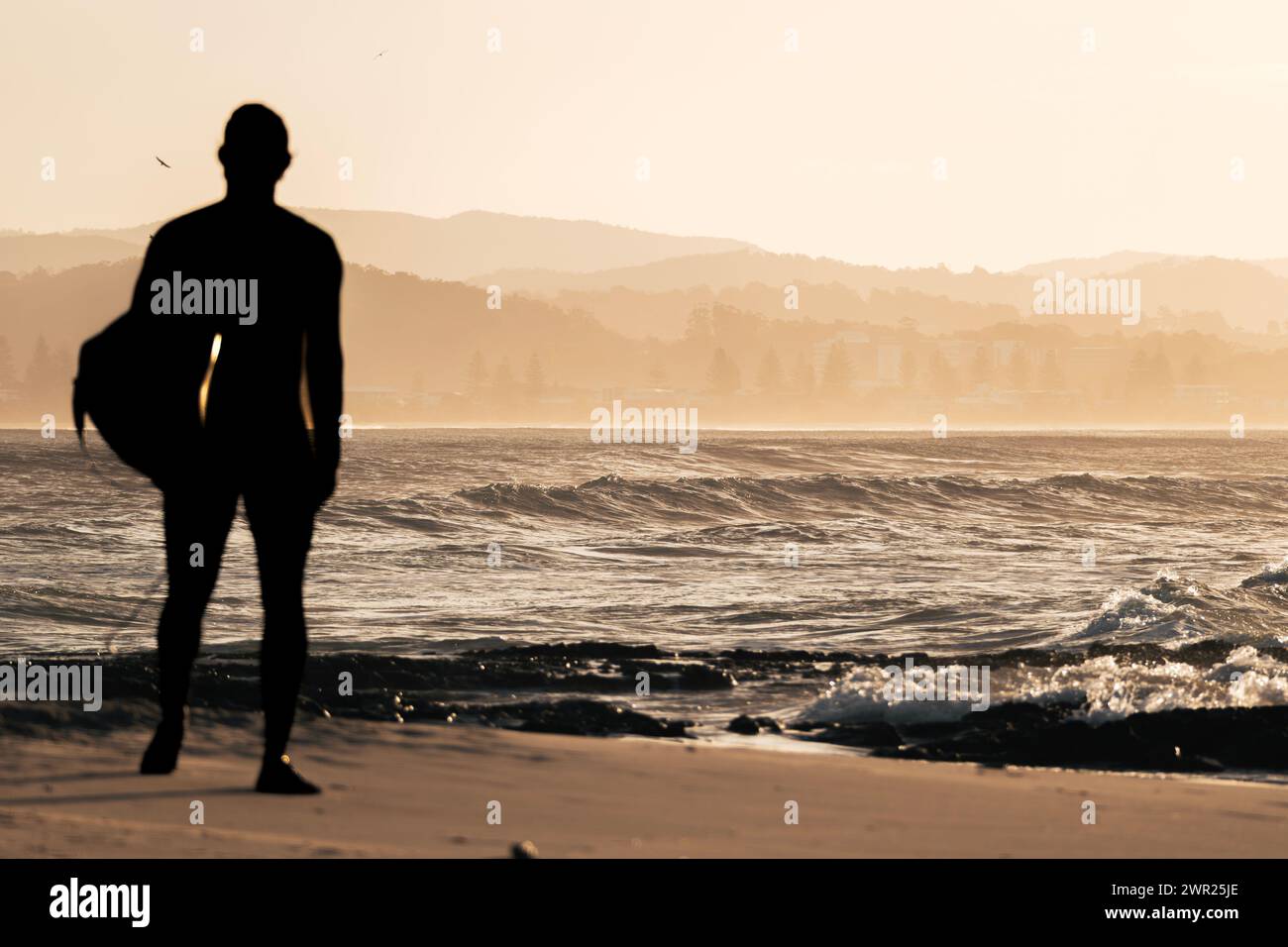 Silhouette of a male surfer walking alone on the beach shore during ...