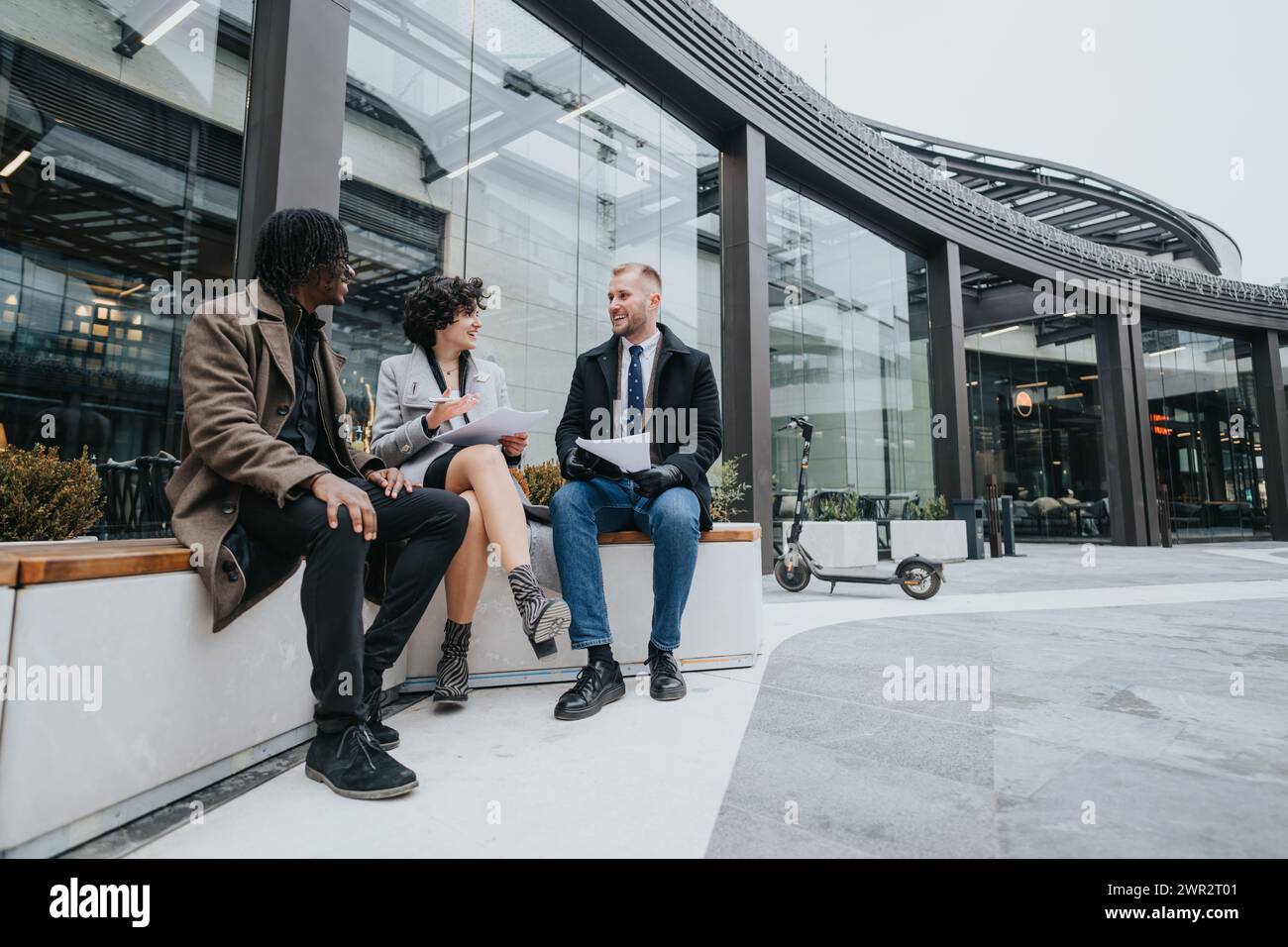 A multiethnic group of business people stands outside a modern building, engaged in a discussion and writing notes in notebook. Stock Photo
