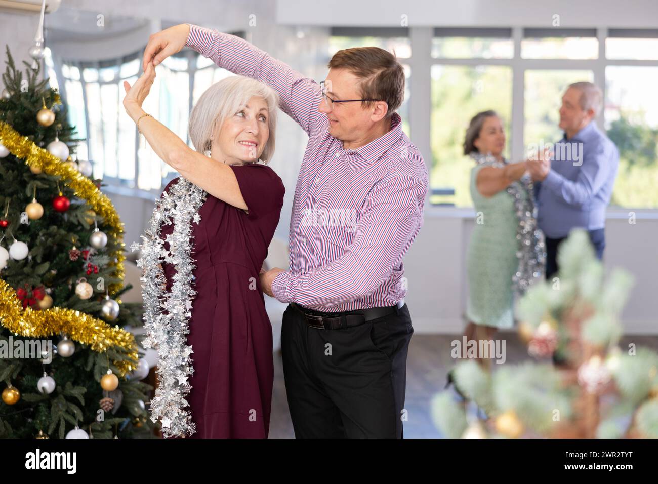 Happy elderly woman and middle-aged male partner successfully perform mesmerizing movements of paso doble dance during celebration Christmas Stock Photo