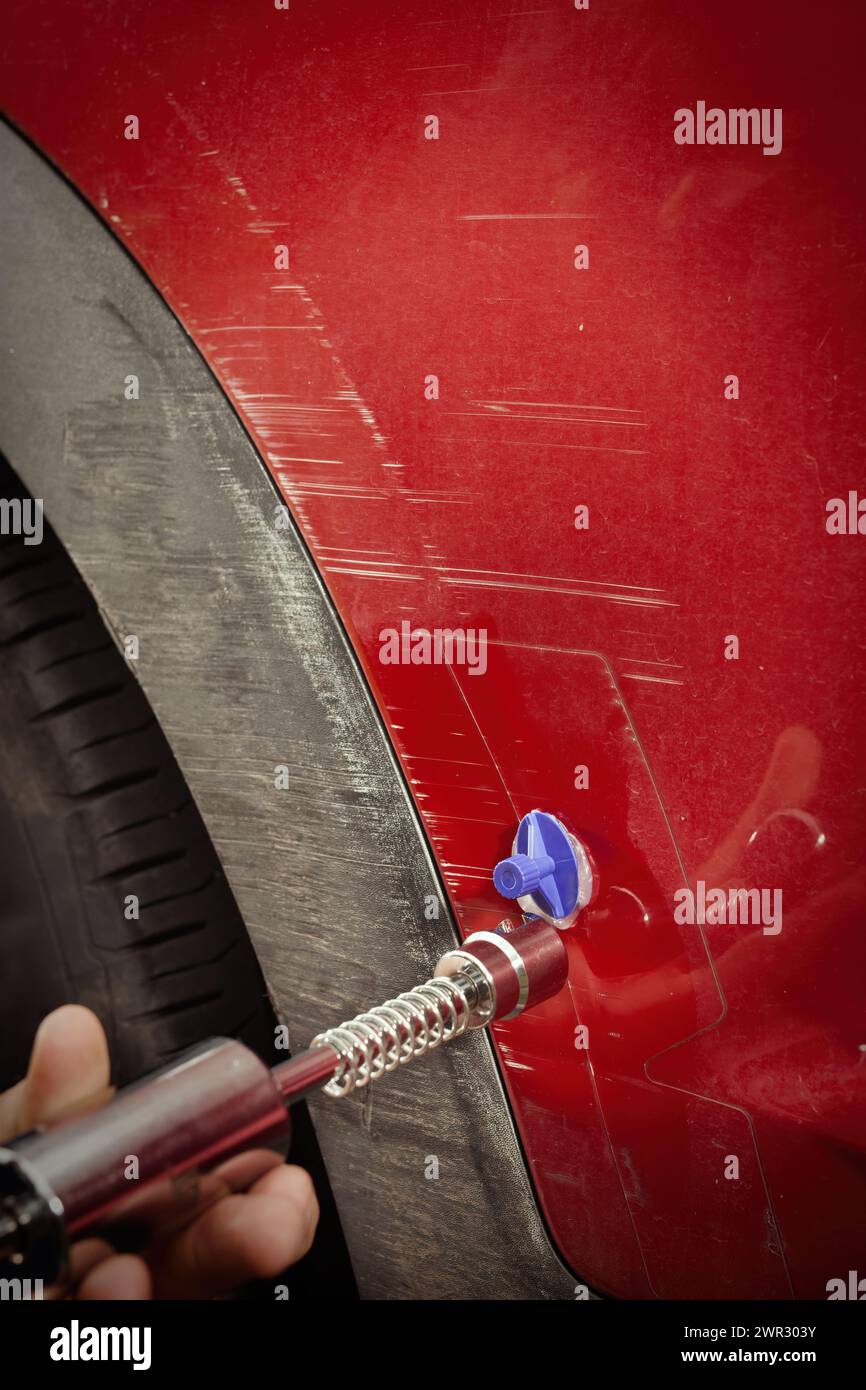 Car owner working on a dent repair with reverse hammer and glue Stock Photo