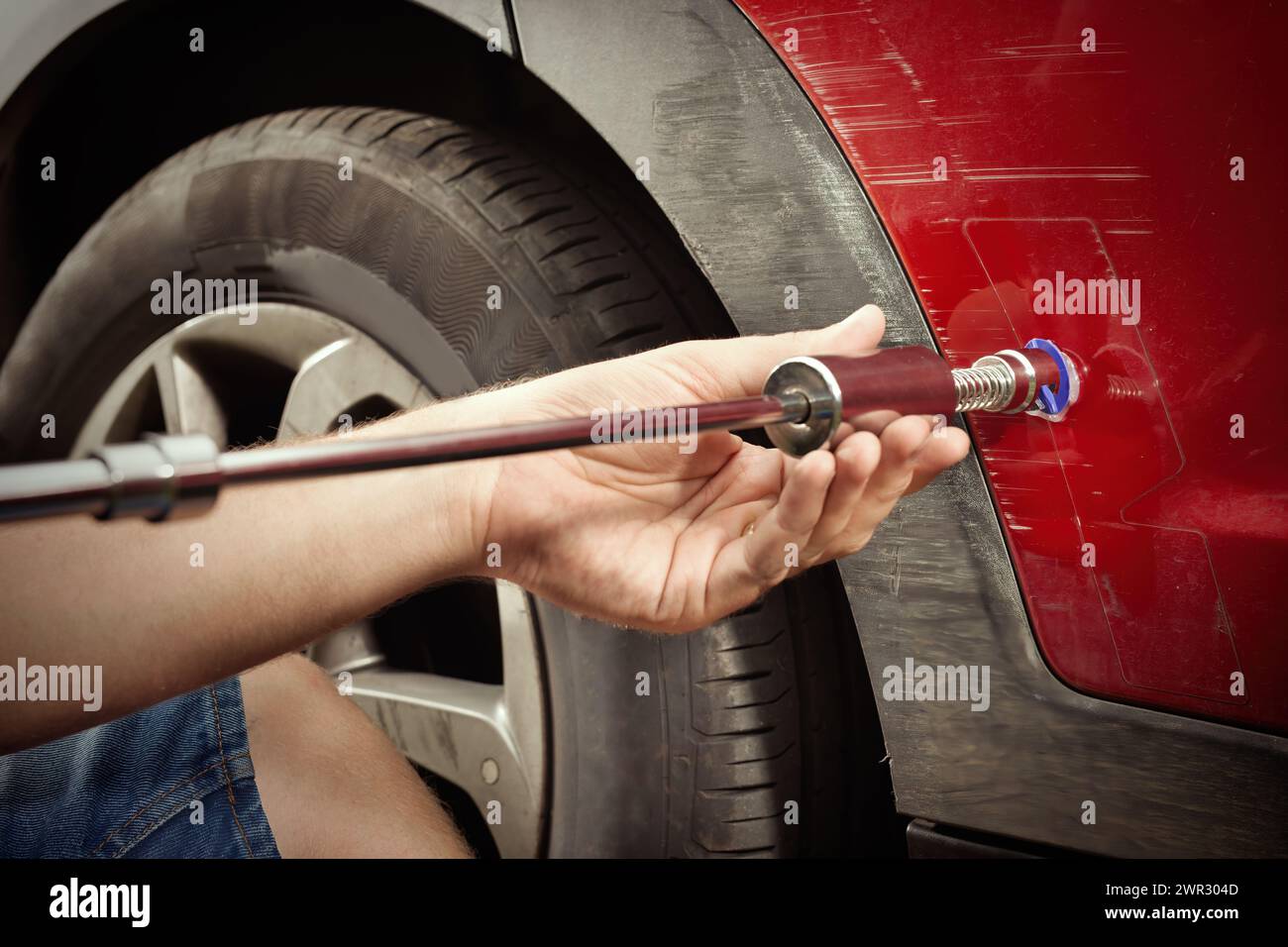 Car owner working on a dent repair with reverse hammer and glue Stock Photo