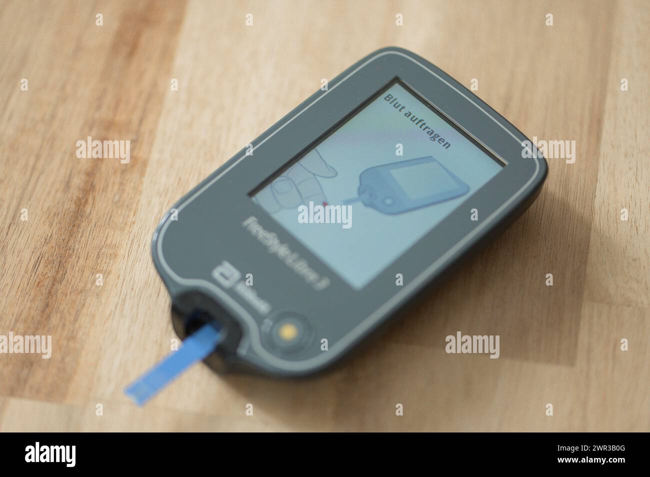 Blood glucose meter with test strips lying diagonally in the centre on a wooden table, ready for a blood glucose measurement, diabetes treatment Stock Photo