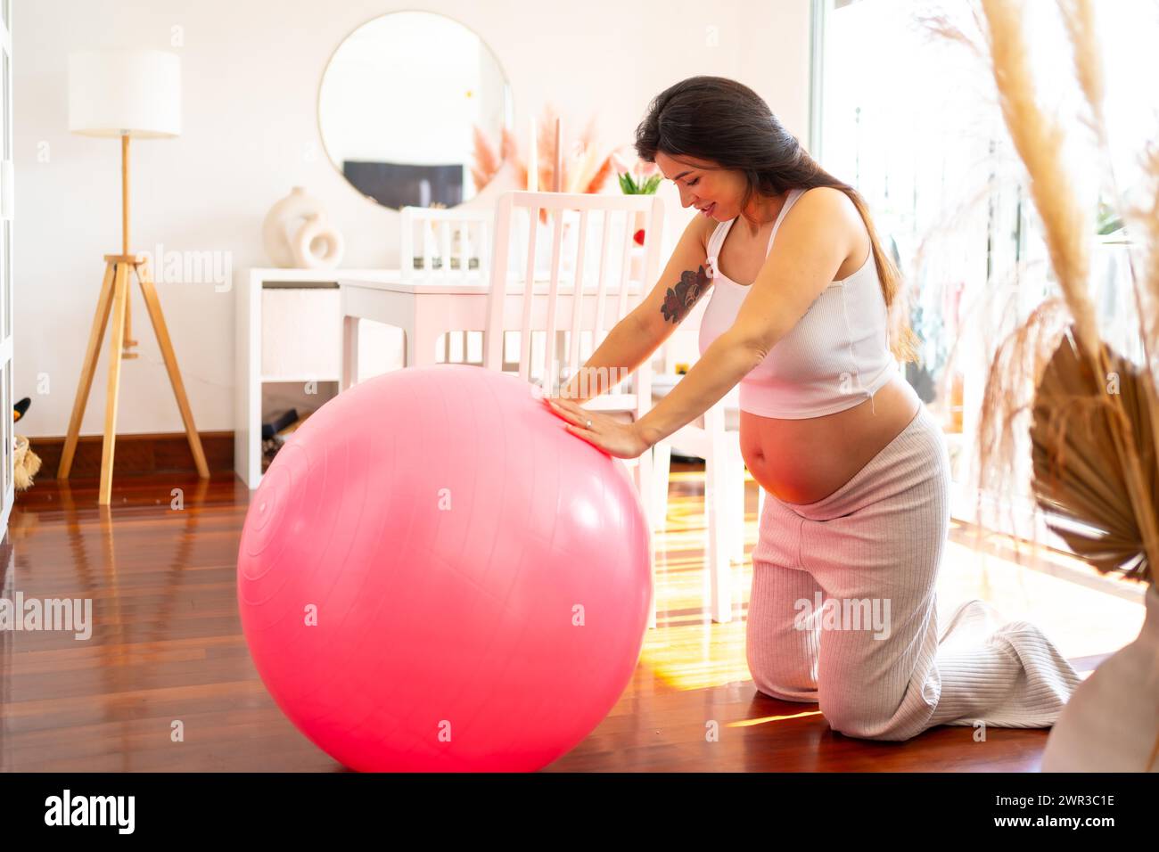 Domestic scene of a beauty pregnant woman using pink pilates ball to exercise at home Stock Photo