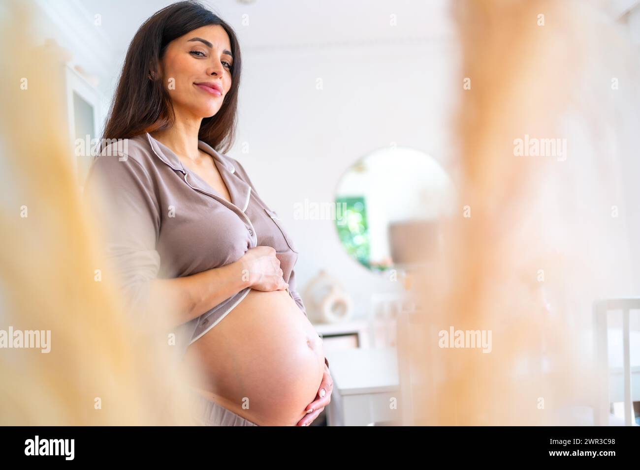 Comfortable beauty pregnant woman standing touching her belly at home Stock Photo
