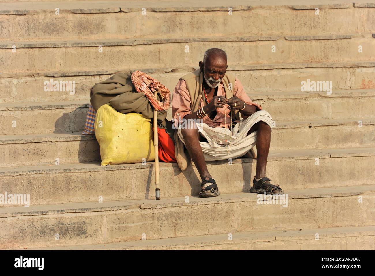 Old man sitting alone on the steps and looking at an object, Varanasi, Uttar Pradesh, India Stock Photo