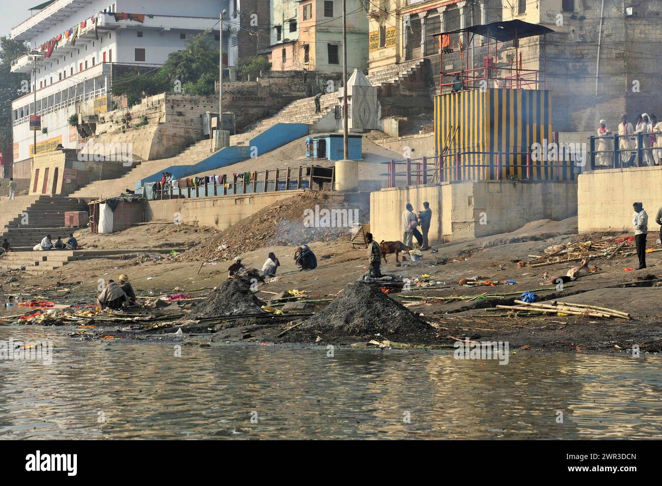 People being cremated near a river, smoke rising and ashes lying on the ground, Varanasi, Uttar Pradesh, India Stock Photo