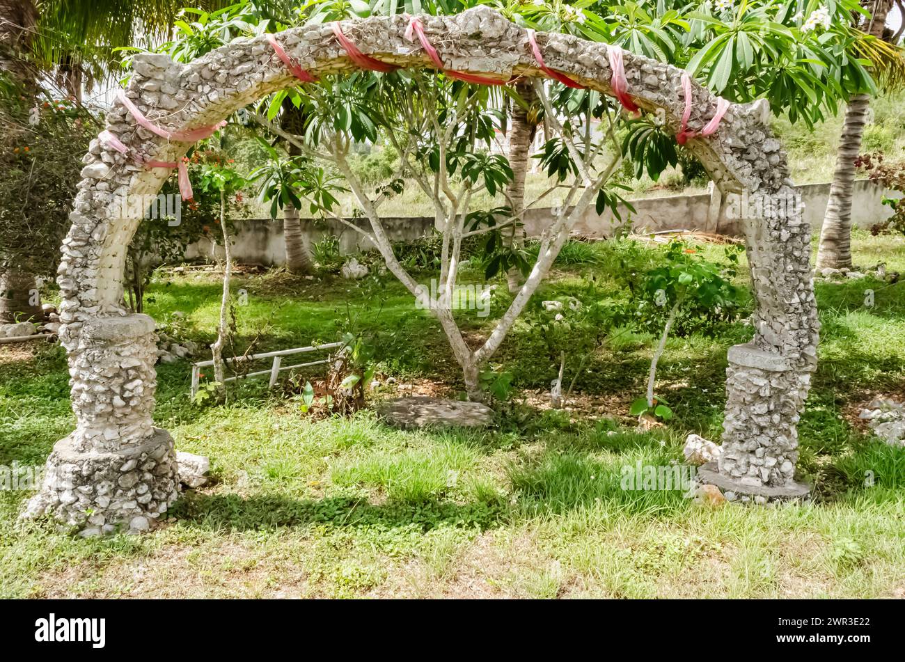 A stone and concrete arch is built on a lawn among trees. Stock Photo