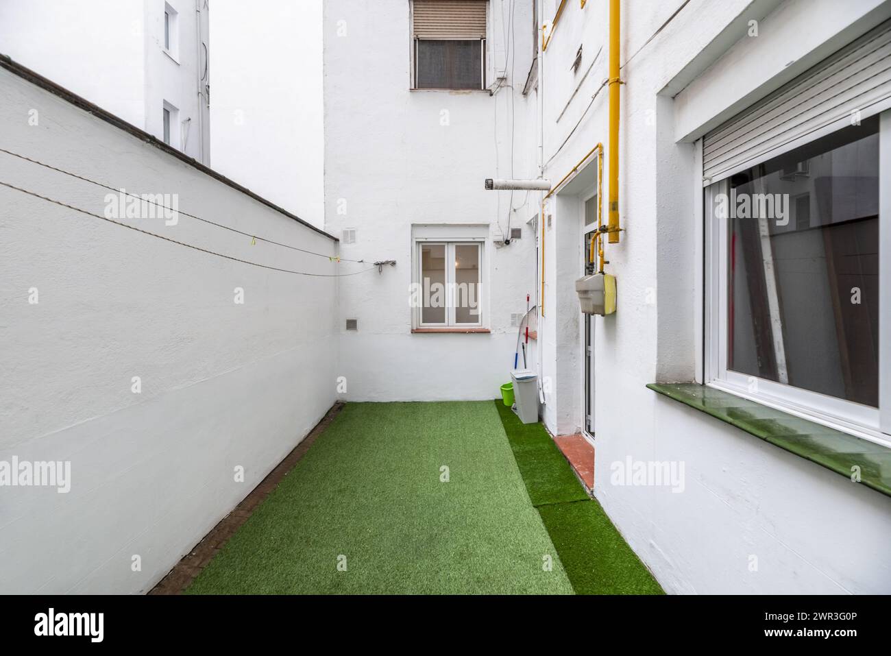 Interior patio of a house with white painted walls, natural gas meter with yellow pipes and artificial grass floors in a ground floor home Stock Photo