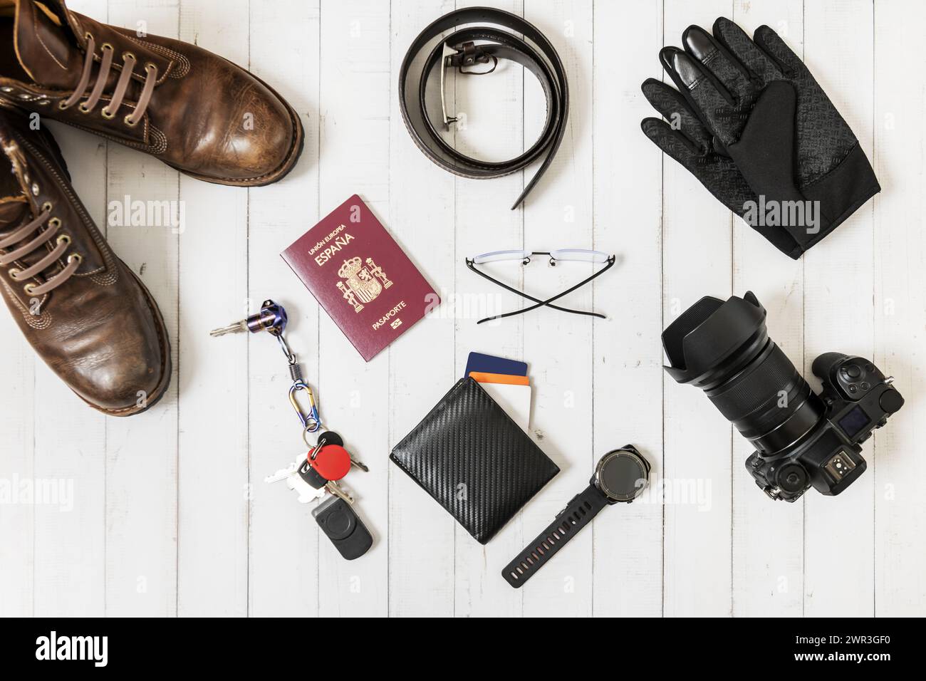 Still life with hiking boots, camera, Spanish passport, carbon fiber wallet and winter gloves on a white surface Stock Photo