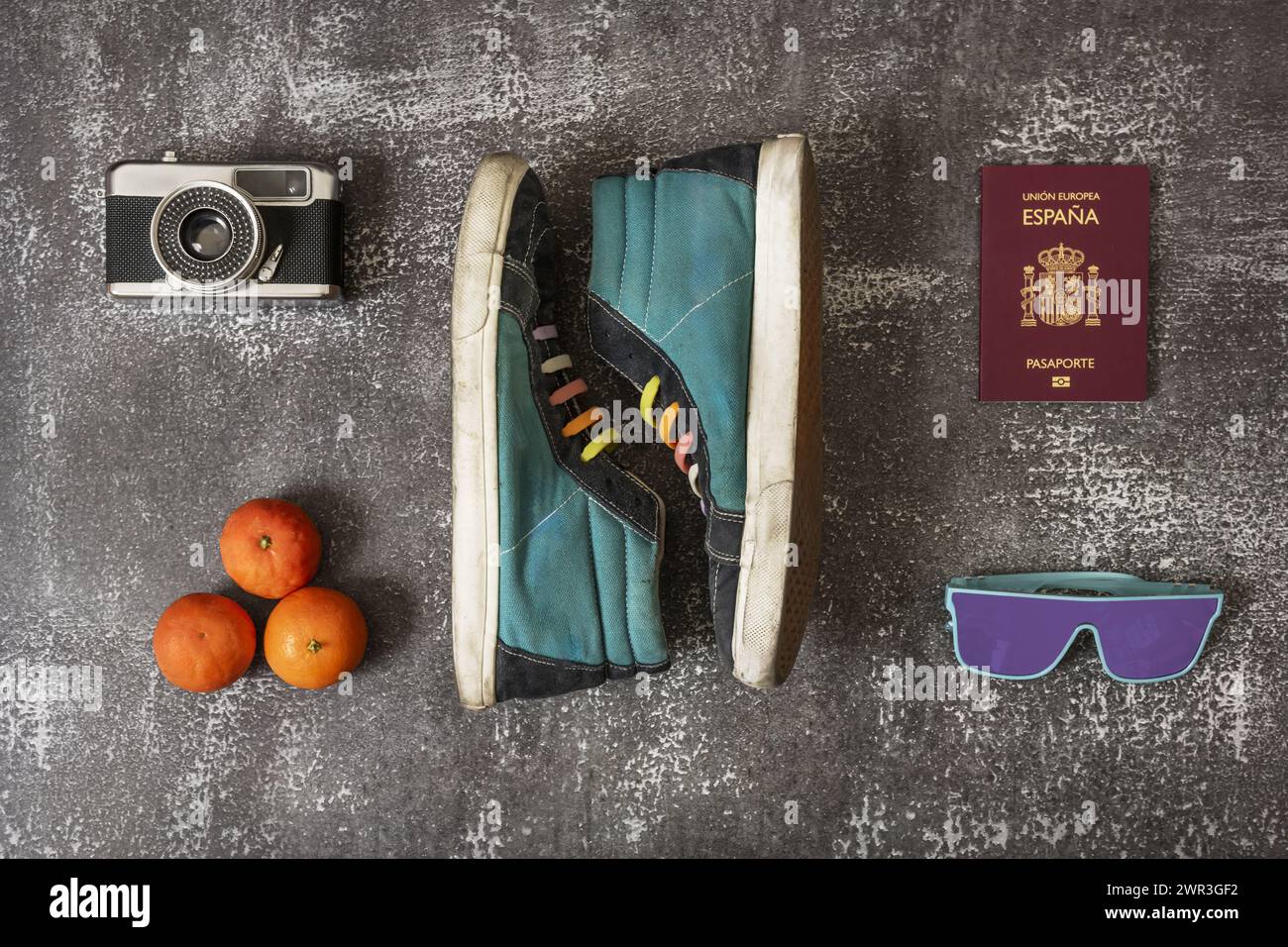 used sports ankle boots with rainbow laces along with an old photo camera, tangerines, Spanish passport and sunglasses on gray surface Stock Photo