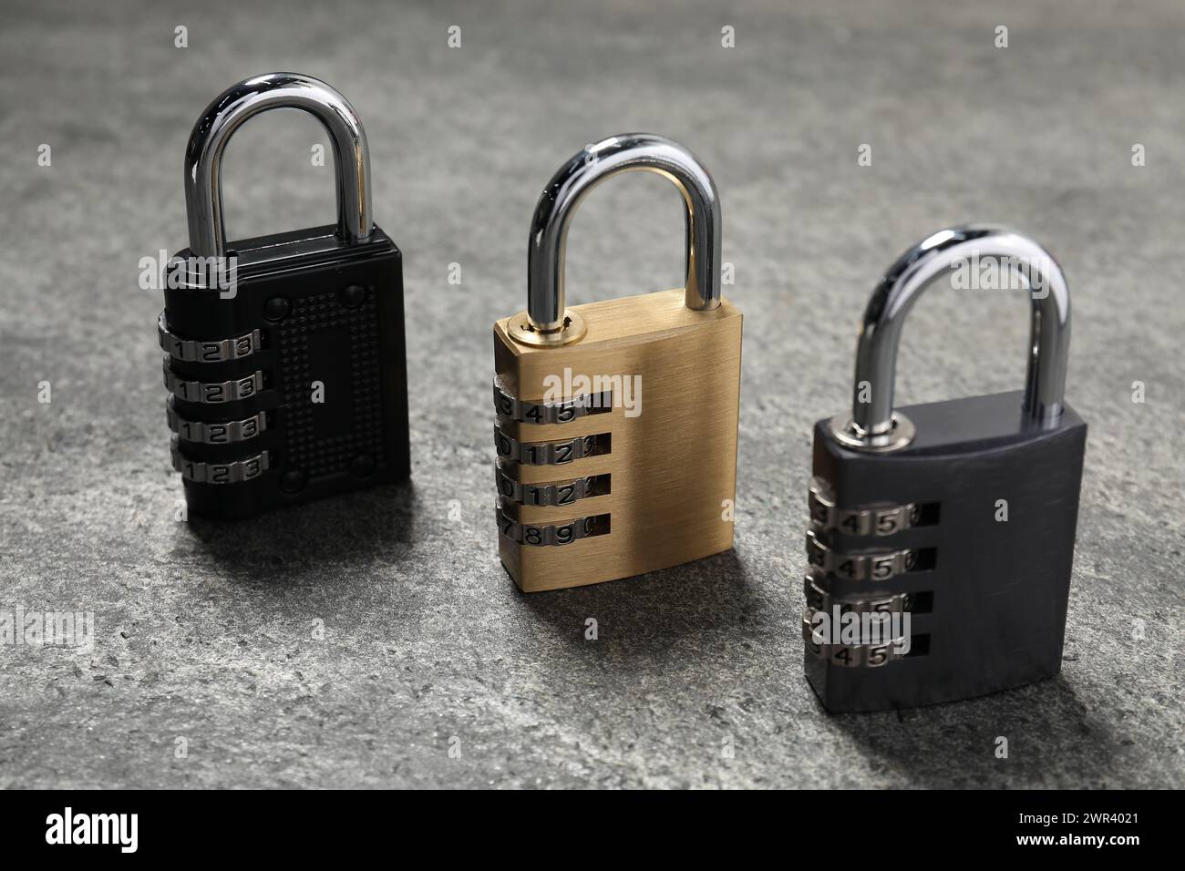 Locked steel combination padlocks on grey stone table, closeup Stock Photo