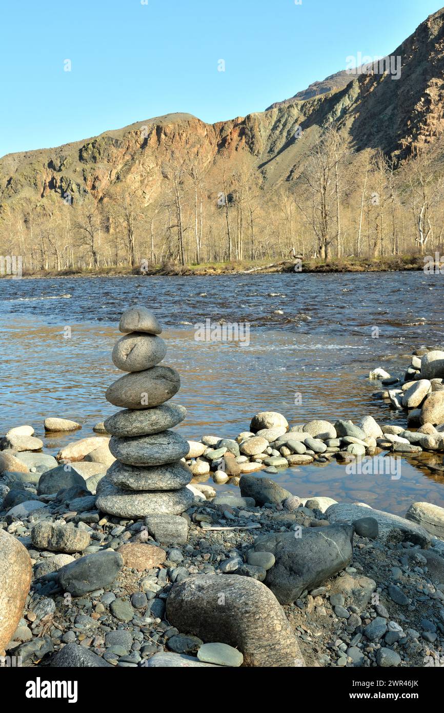 A small stone pyramid on the bank of a stormy mountain river on a sunny spring day. Chulyshman river, Altai, Siberia, Russia. Stock Photo