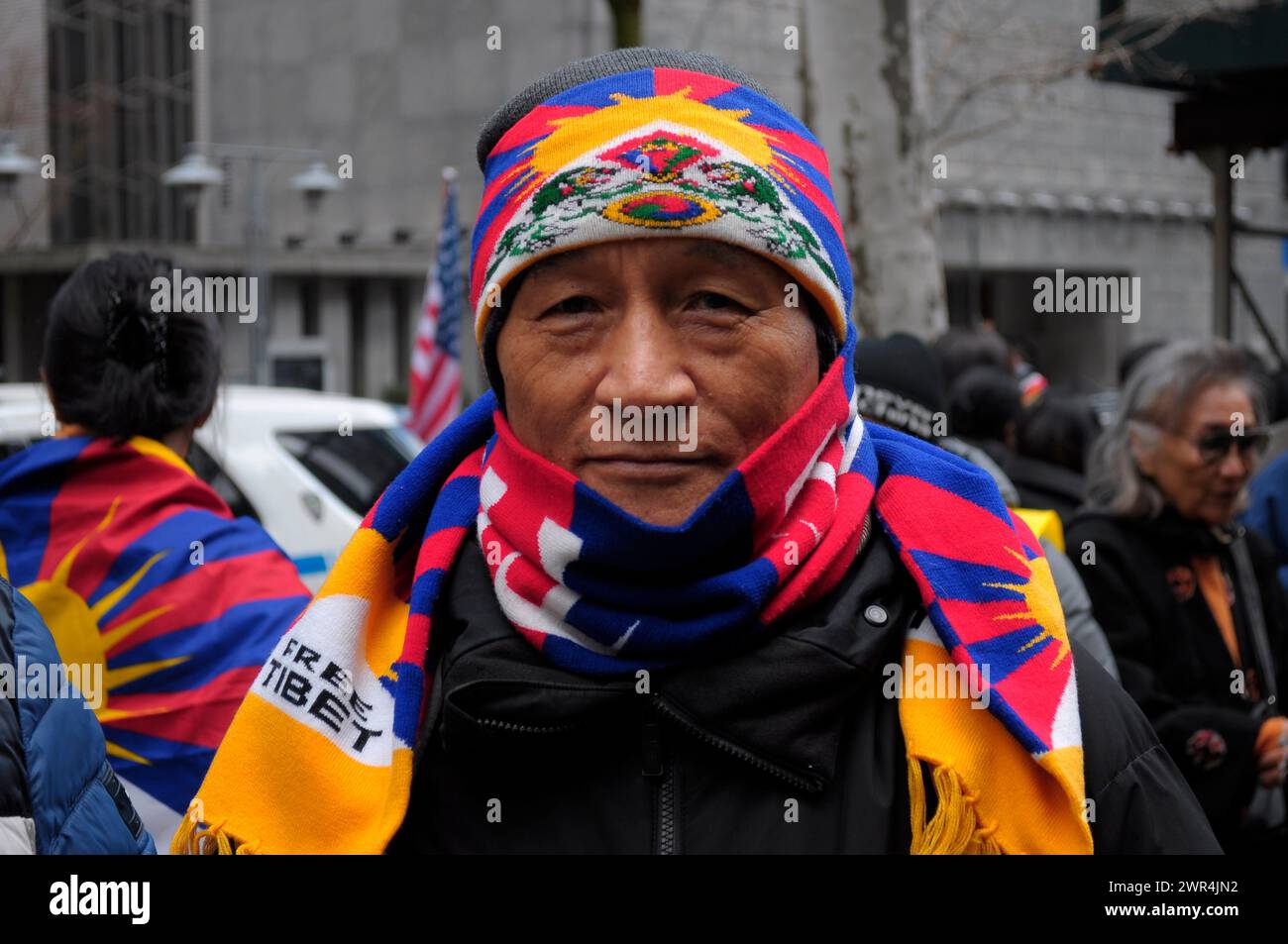 A pro-Tibet demonstrator wearing the colors of the Tibetan flag rallies at Dag Hammarskjöld Plaza near the United Nations building during the 65th Tibetan Uprising Day. Demonstrators rallied in Manhattan, New York City demanding Tibet's independence from China. The Tibetan Uprising Day marks the day in 1959 when thousands of Tibetans in Tibet surrounded the palace of the current and 14th Dalai Lama. The Dalai Lama is the spiritual Buddhist leader of Tibetans worldwide. The Tibetans surrounded the palace in 1959 to protect the Dalai Lama due to fears of a Chinese government plot to abduct him. Stock Photo