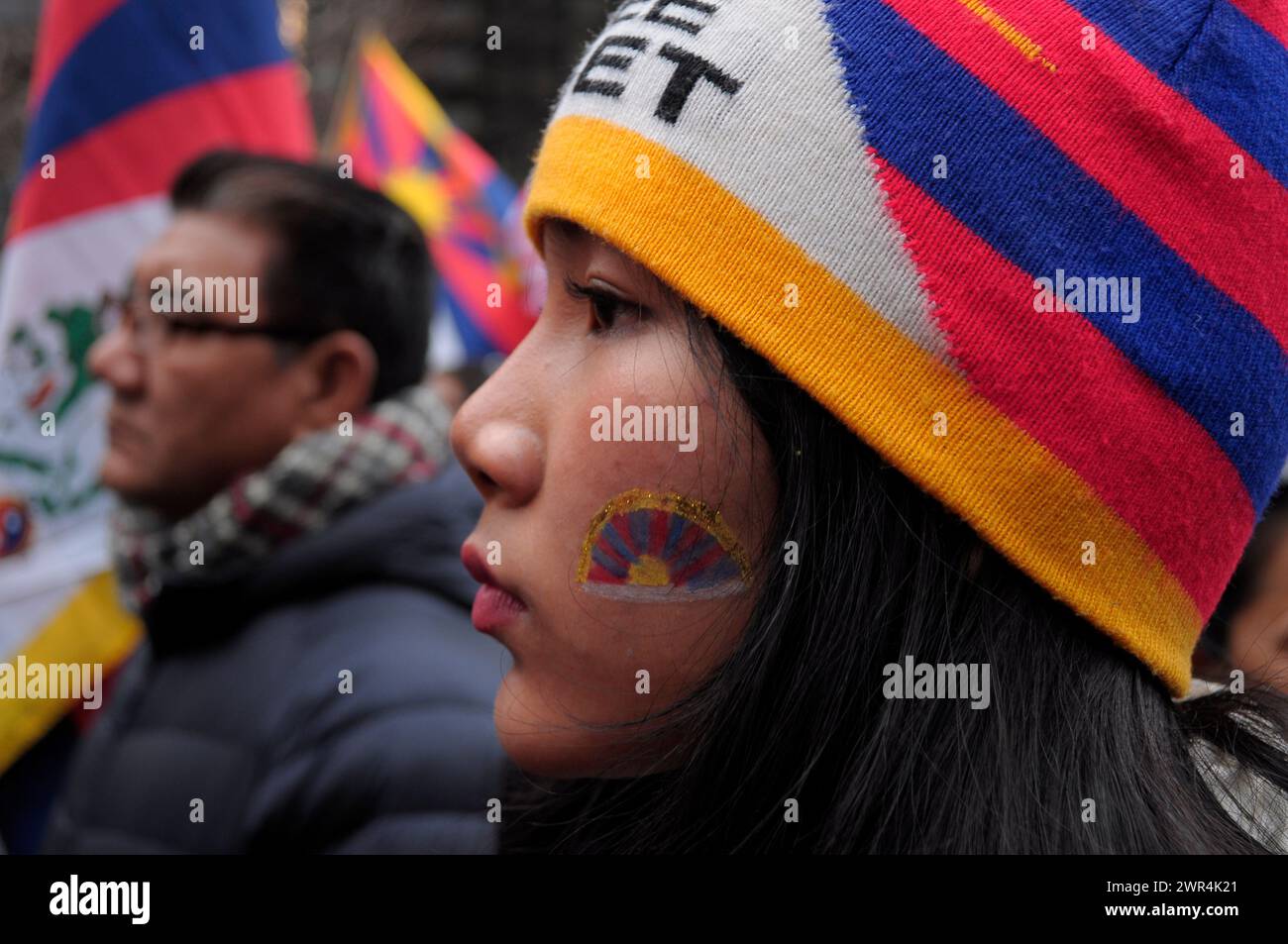 A pro-Tibet demonstrator with the Tibetan flag painted on her cheek, rallies at Dag Hammarskjöld Plaza near the United Nations building during the 65th Tibetan Uprising Day. Demonstrators rallied in Manhattan, New York City demanding Tibet's independence from China. The Tibetan Uprising Day marks the day in 1959 when thousands of Tibetans in Tibet surrounded the palace of the current and 14th Dalai Lama. The Dalai Lama is the spiritual Buddhist leader of Tibetans worldwide. The Tibetans surrounded the palace in 1959 to protect the Dalai Lama due to fears of a Chinese government plot to abduct Stock Photo