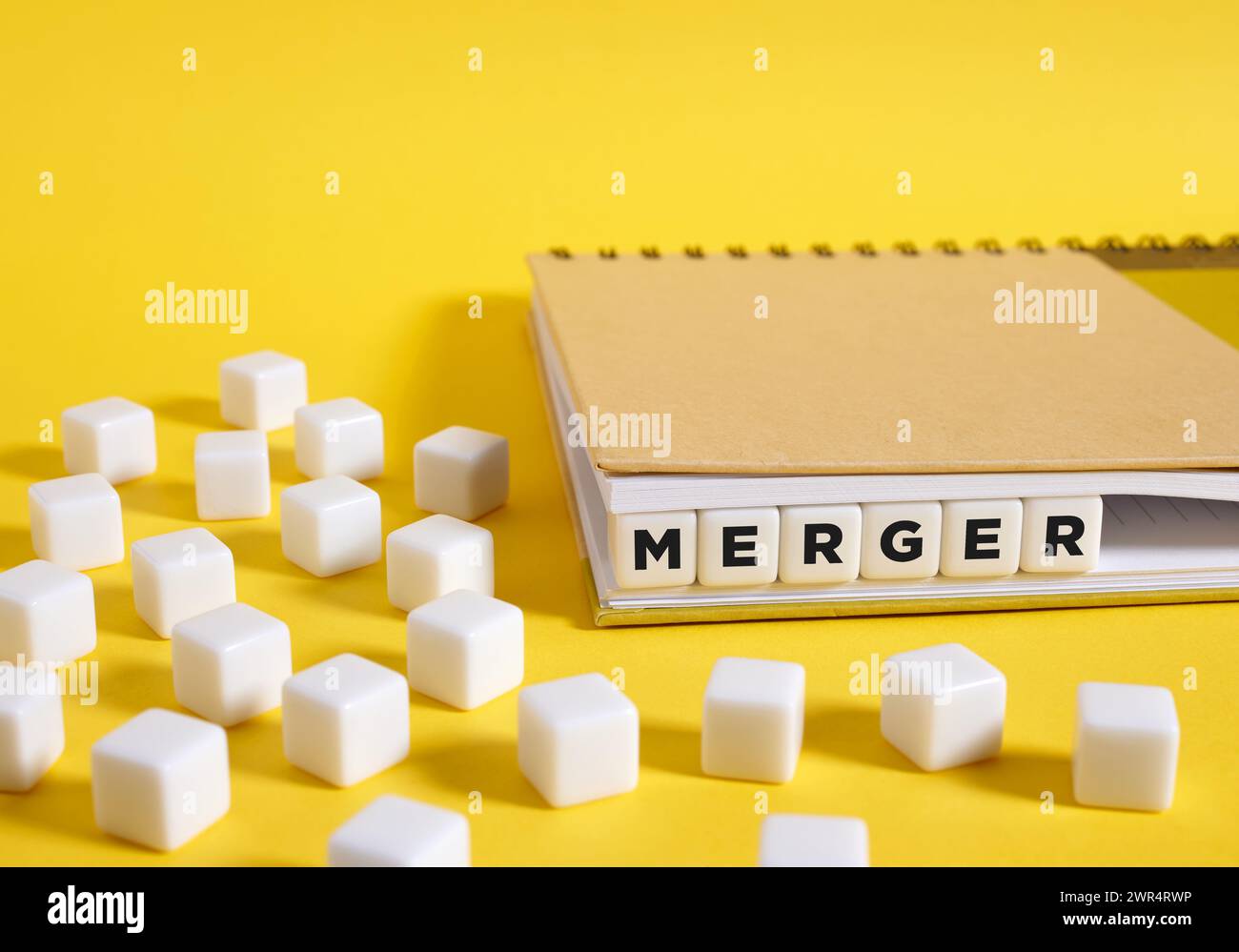 The word merger written on cubes in a notebook on yellow background. Business Merger and Acquisitions concept. Stock Photo