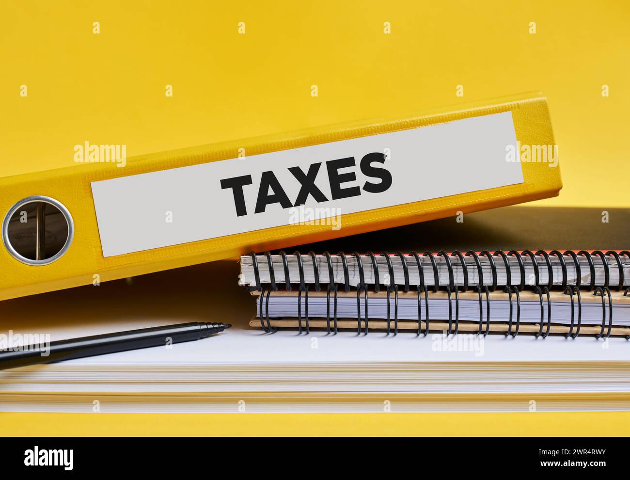 The word taxes written on the label of a yellow binder on the office desk. Stock Photo