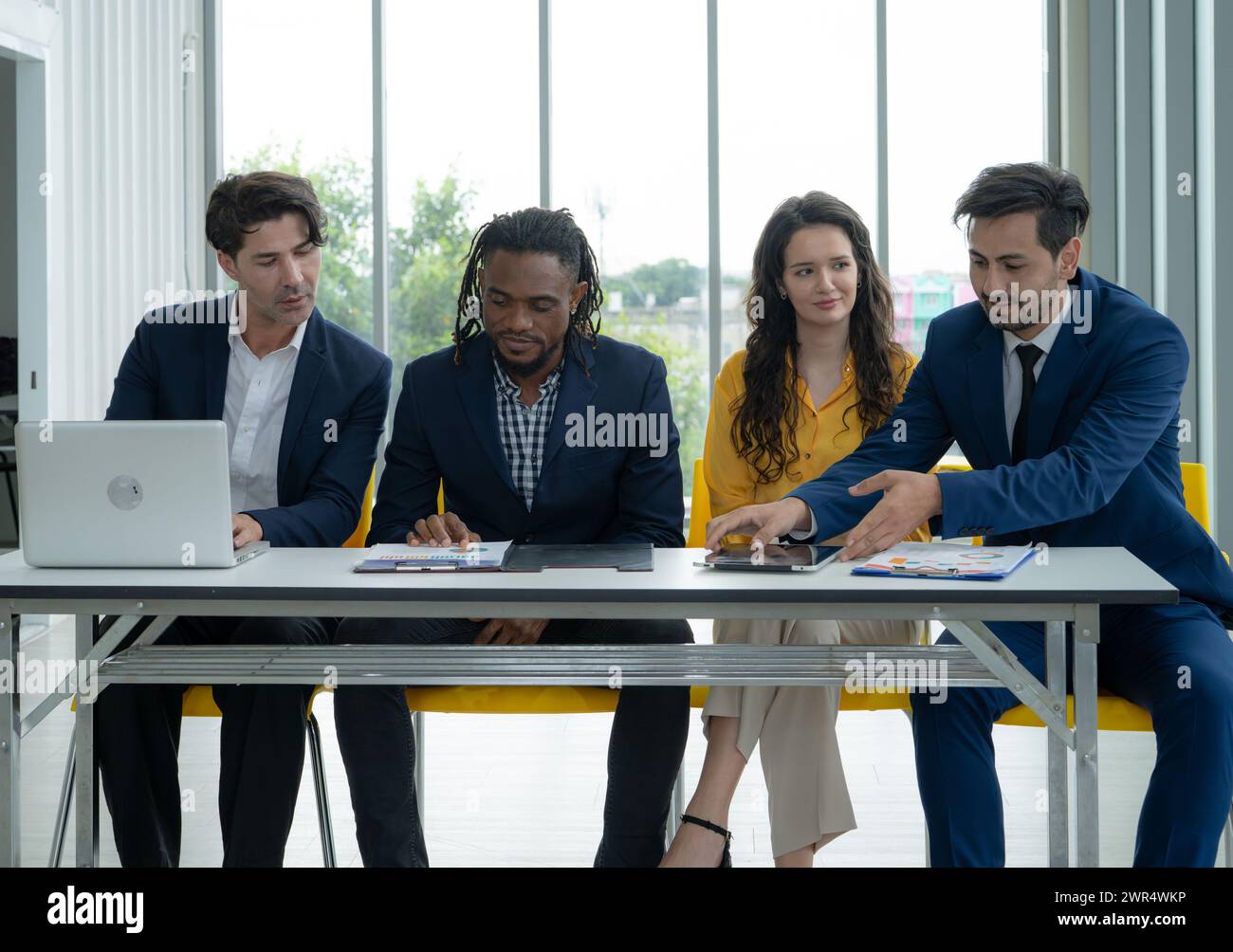 A group of people are sitting around a table with a laptop and papers ...