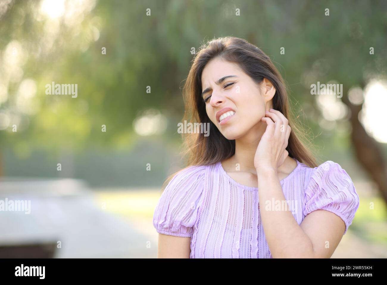 Stressed woman scratching neck standing in a park Stock Photo