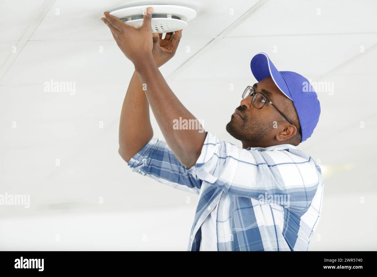 worker installing smoke detector on the ceiling Stock Photo